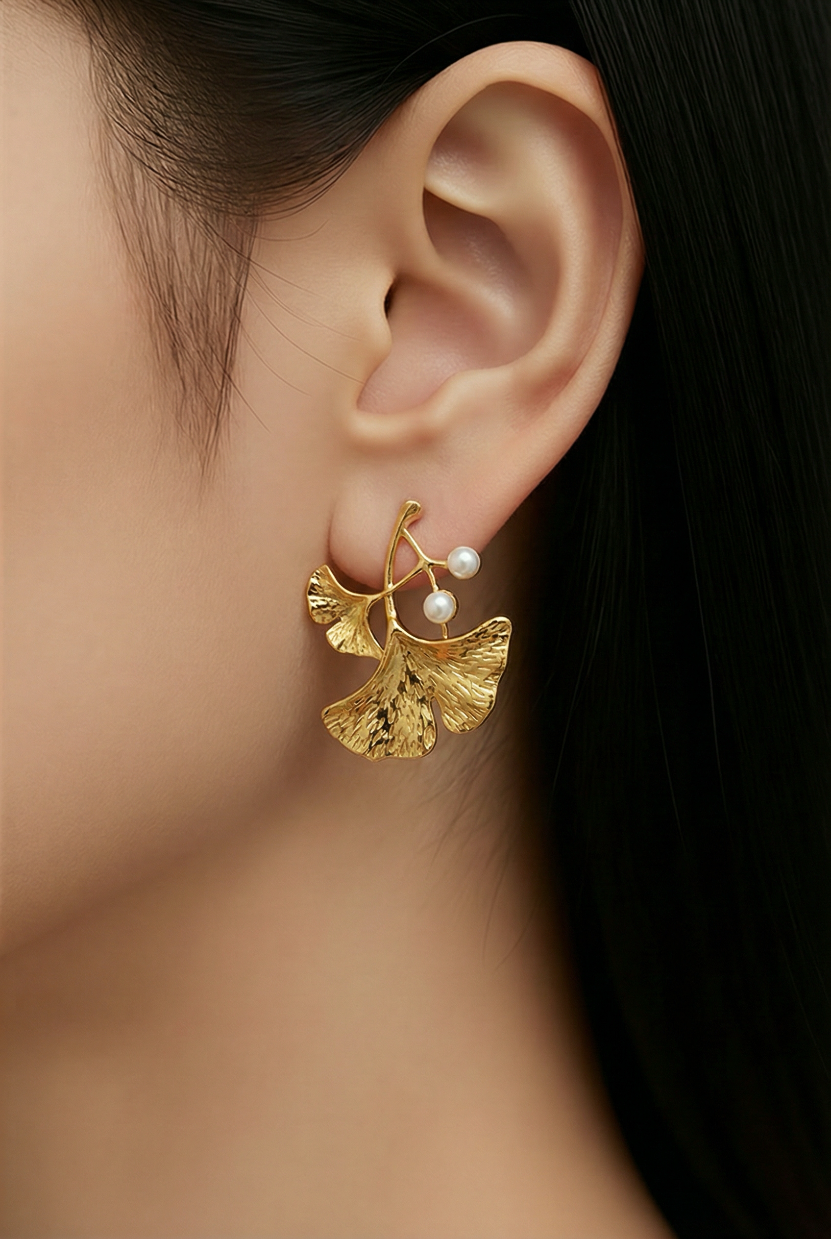 Gold leaf earring with pearl detail worn by a person