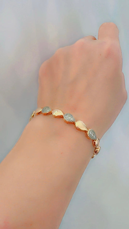 Gold bracelet with drop-shaped stones on a wrist against a light gray background