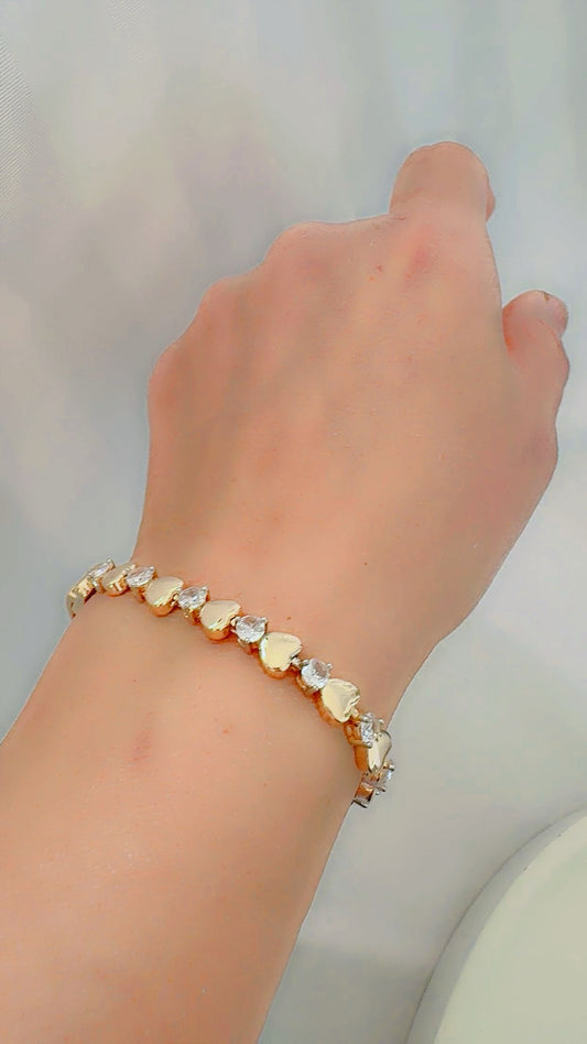 Hand wearing a bracelet with heart-shaped charms on a neutral background