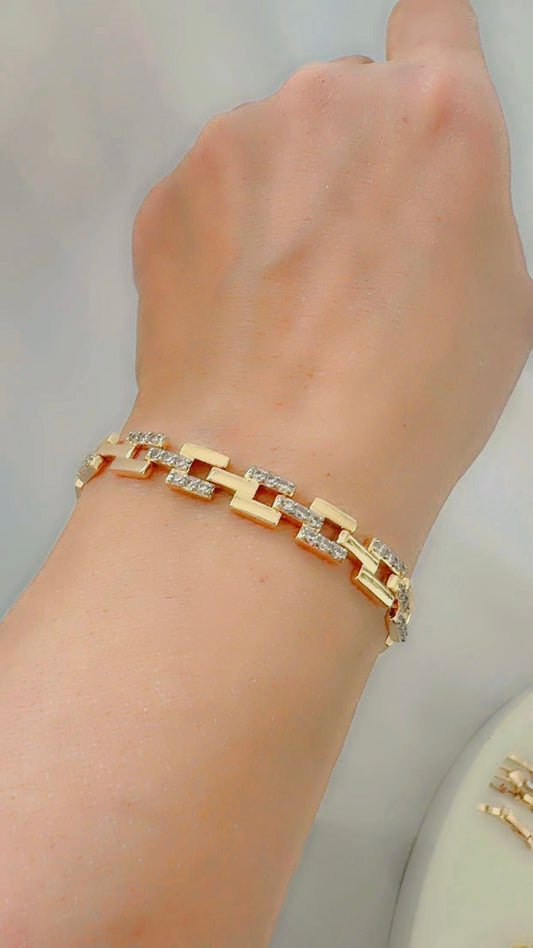 Gold bracelet with zircon on a wrist against a neutral background