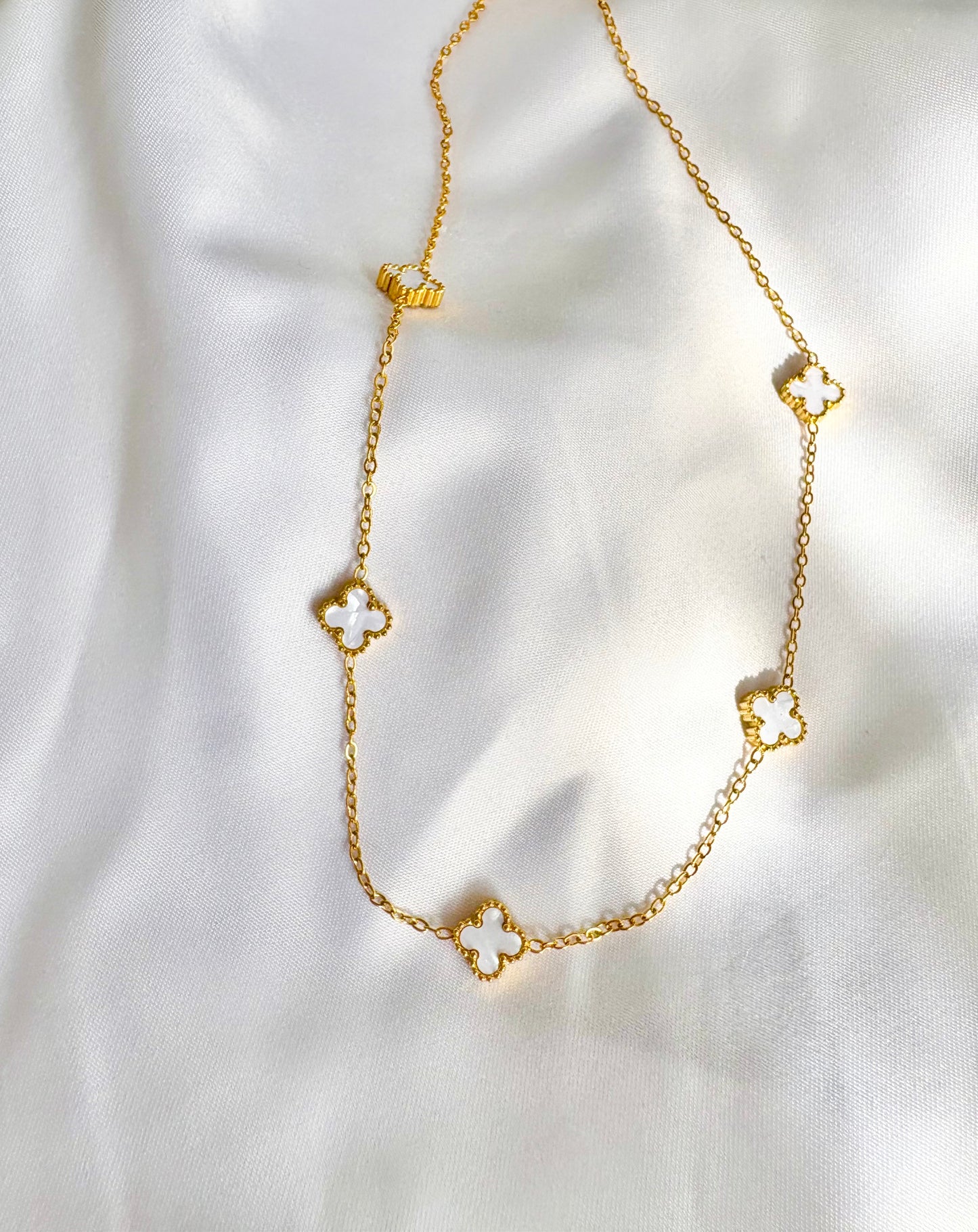 Gold necklace with clover-shaped charms on a white fabric background