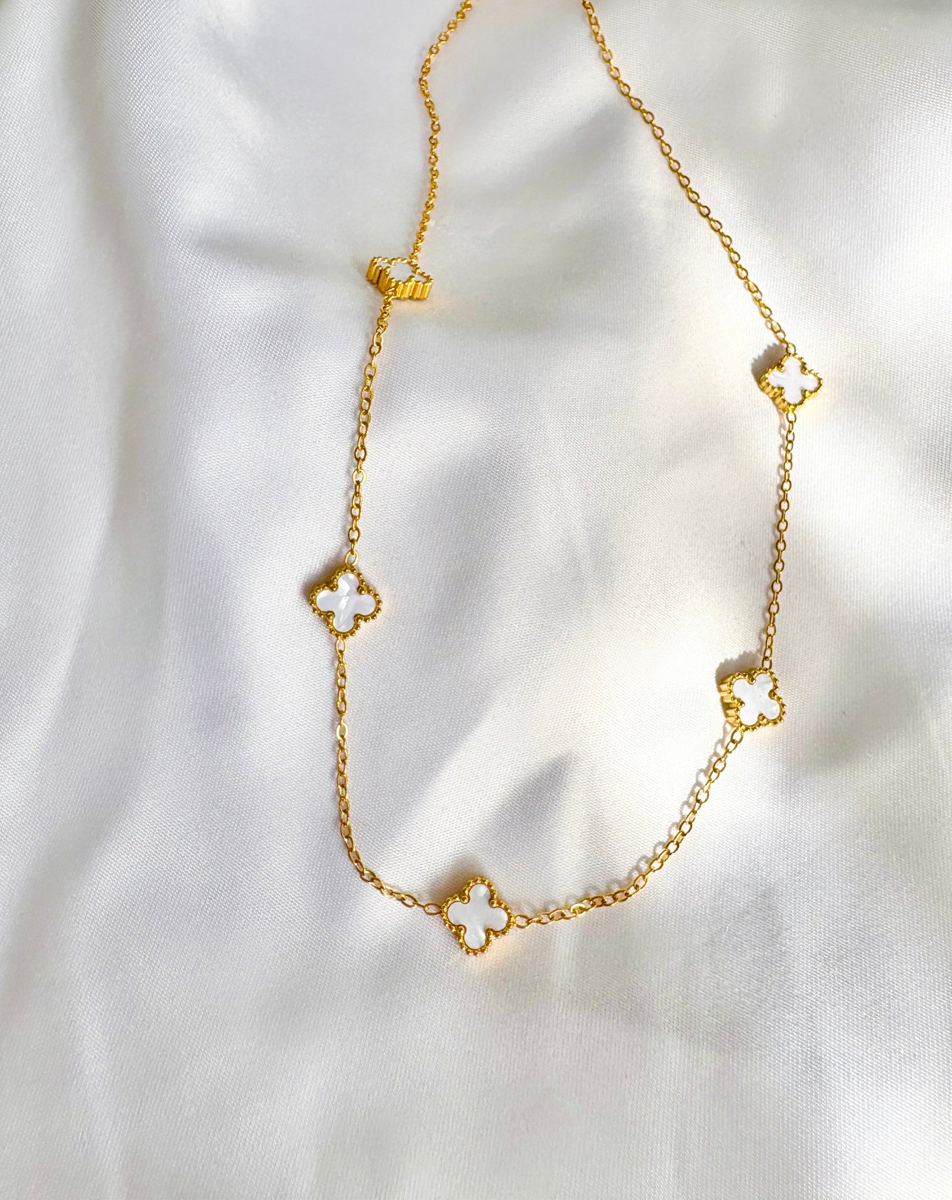 Gold necklace with clover-shaped charms on a white fabric background