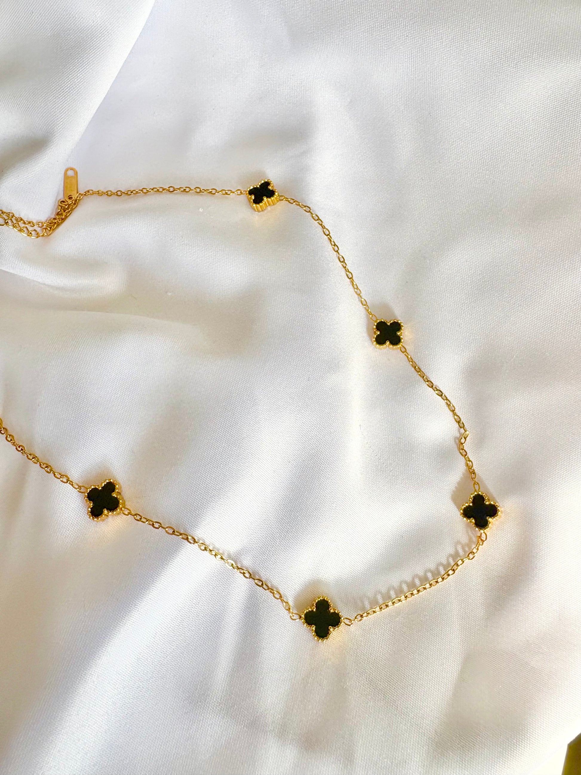 Gold necklace with black clover pendants on a white fabric background