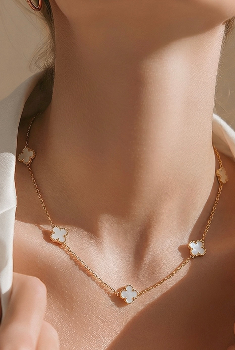 Necklace with white clover pendants on a person wearing a white top.