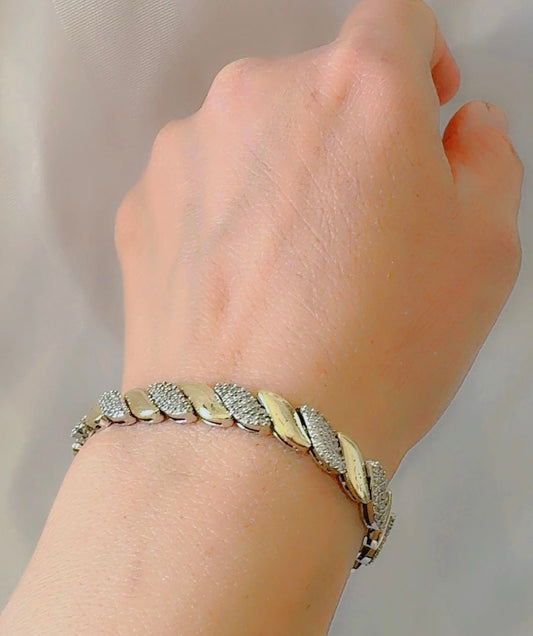 Hand wearing a bracelet with leaf designs on a neutral background