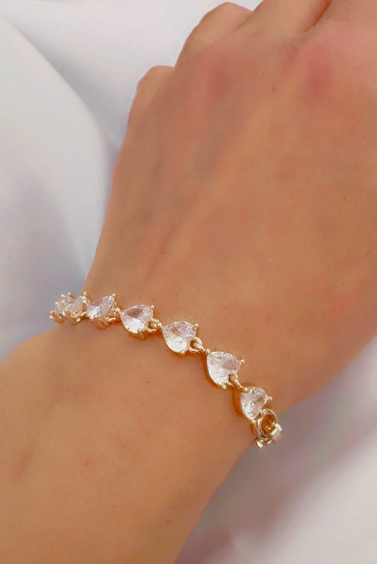 Gold bracelet with clear heart stones on a wrist against a white background