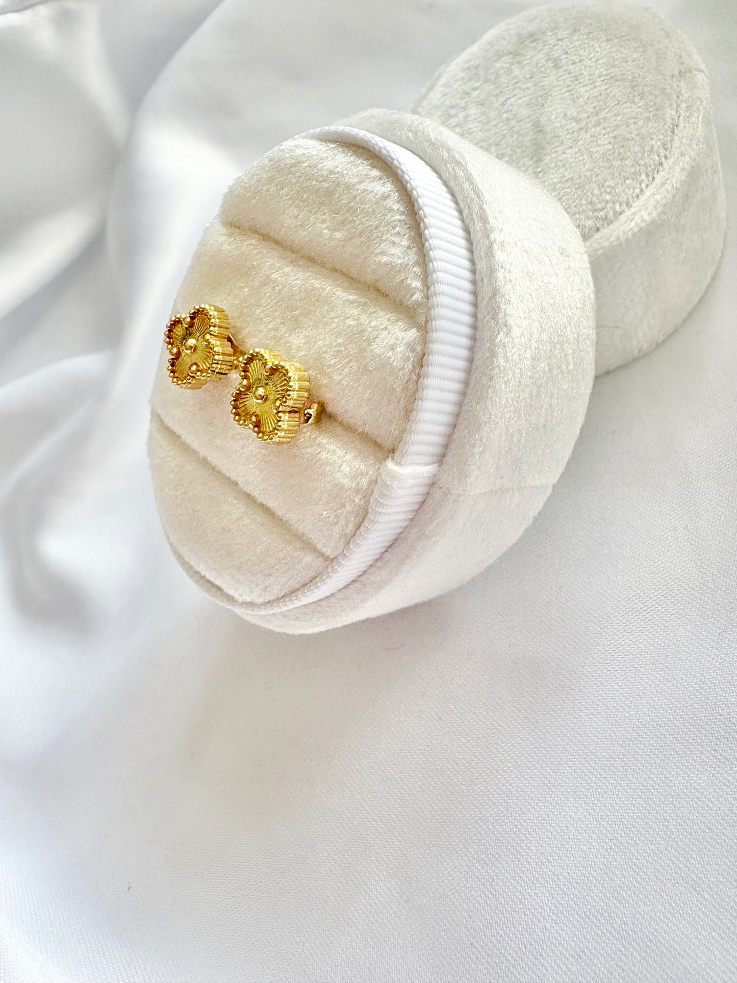 Gold clover earrings in a white jewelry box on a white fabric background