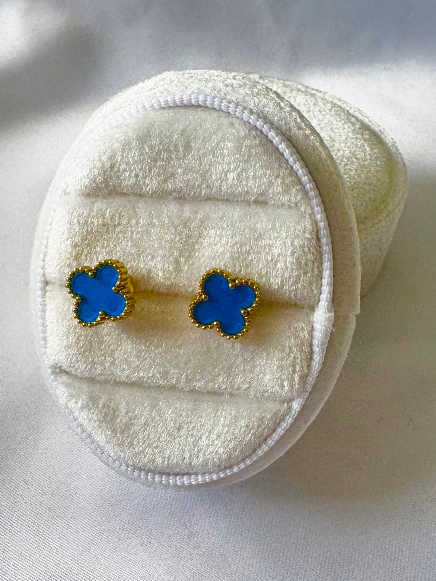 Blue clover earrings on a white textured surface