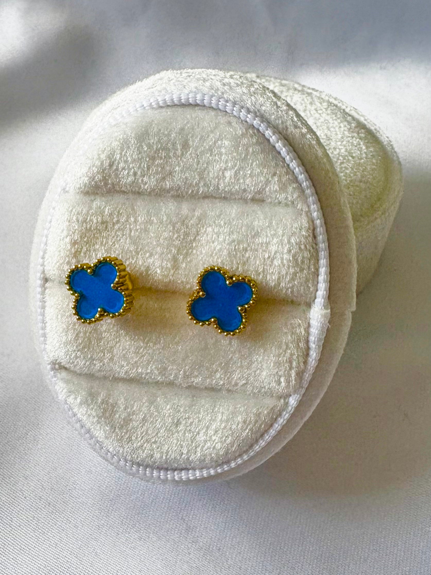 Blue clover earrings on a white textured surface