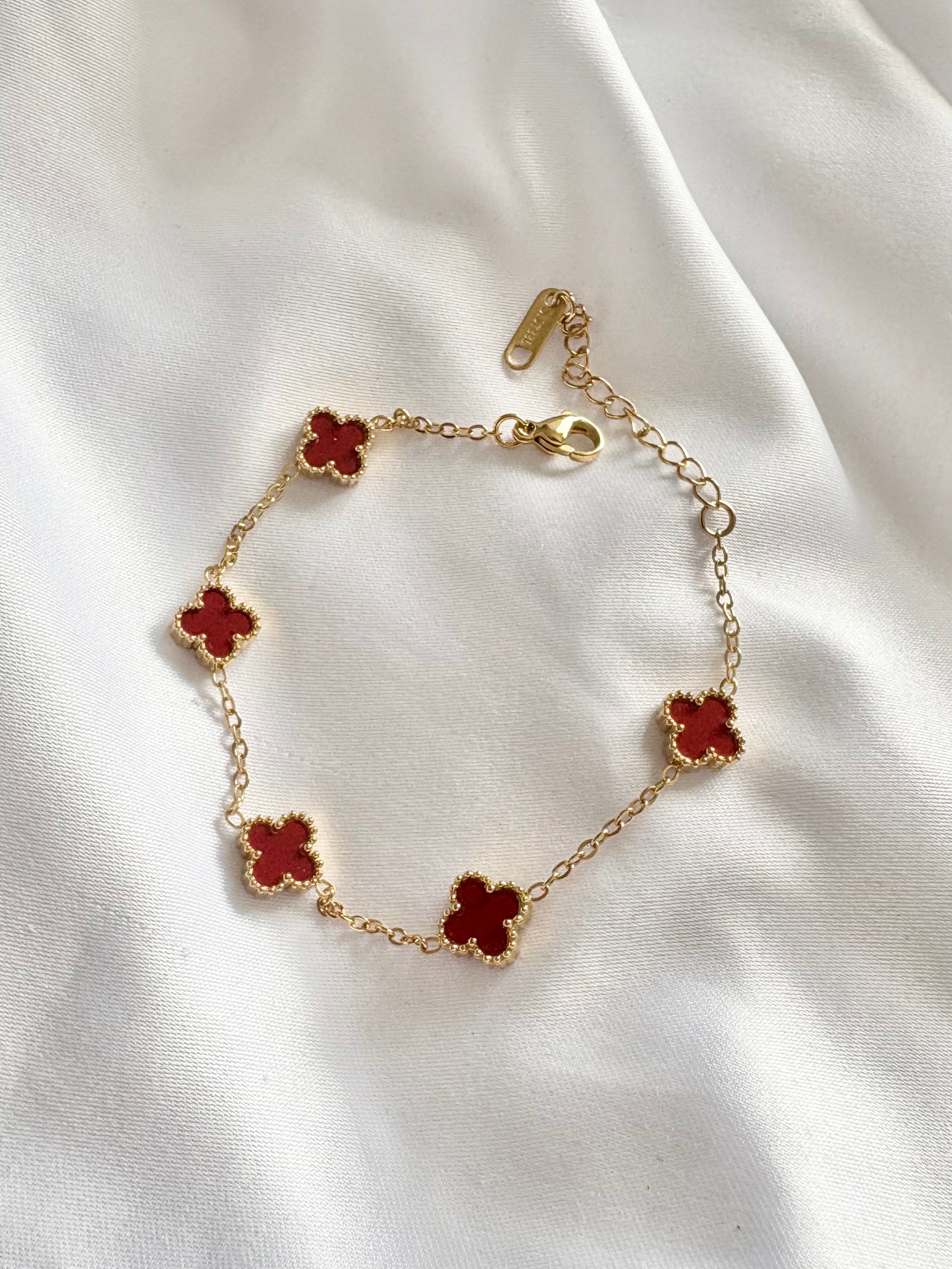 Gold bracelet with red wine clover charms on a white fabric background