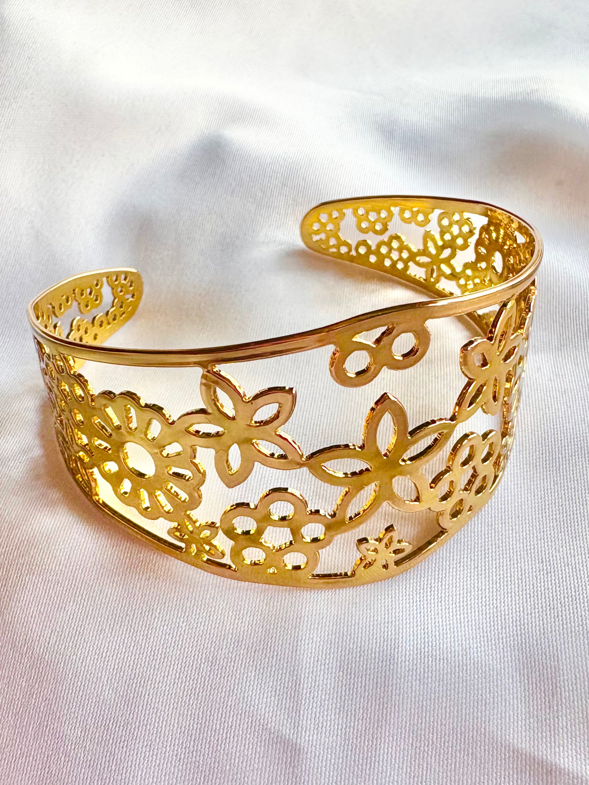 Gold bracelet with floral cut-out design on a white fabric background