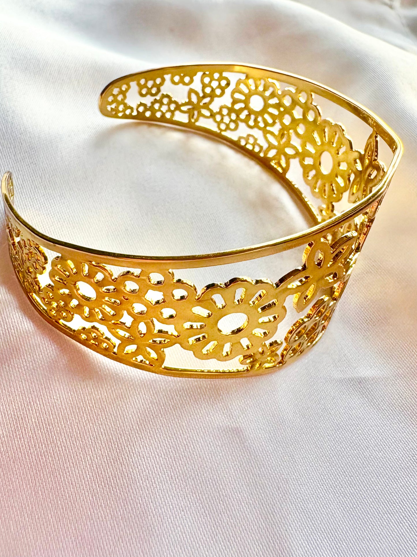Gold bracelet with intricate floral design on a white fabric background