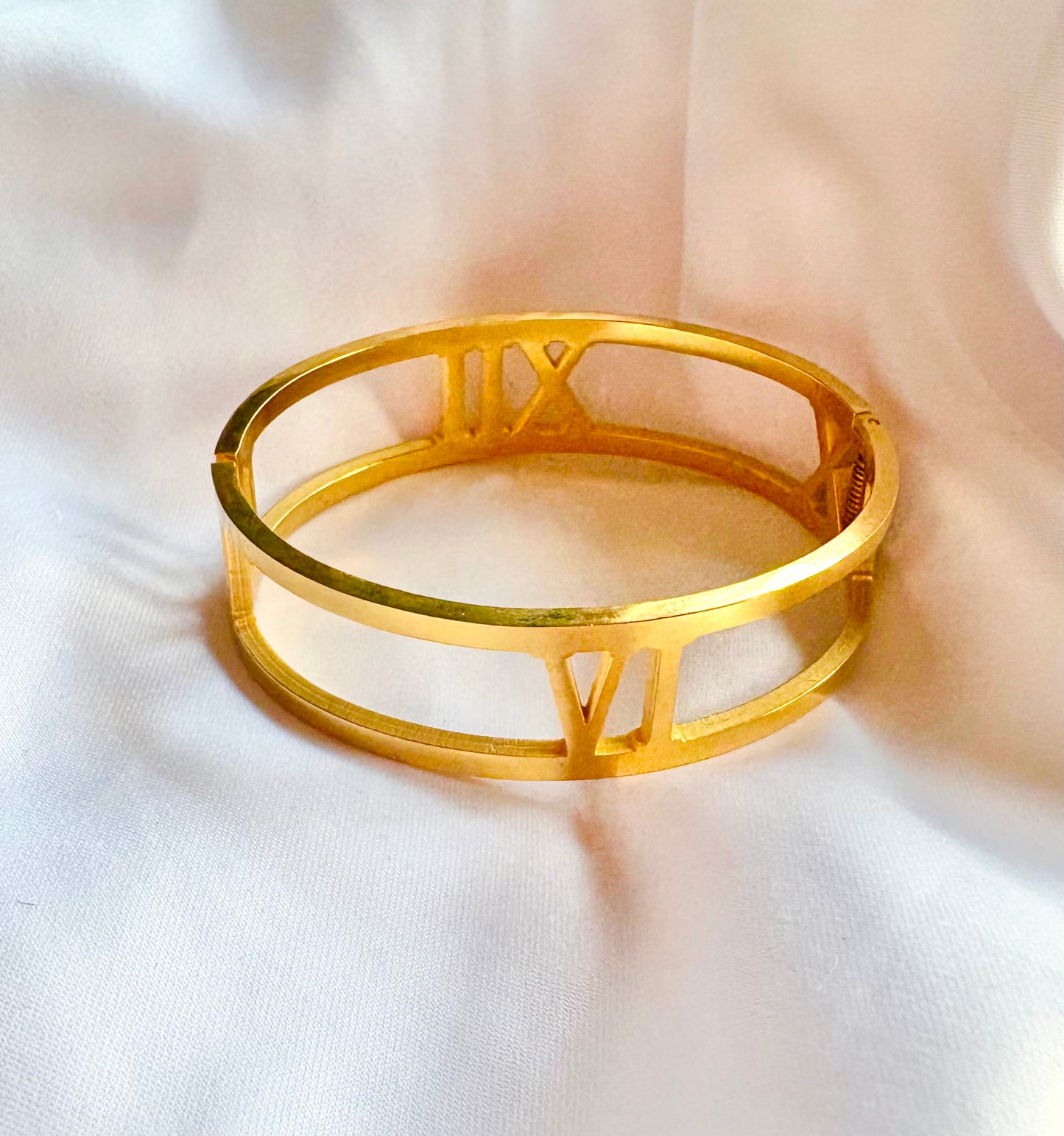 Gold bracelet with Roman numeral design on a white fabric background