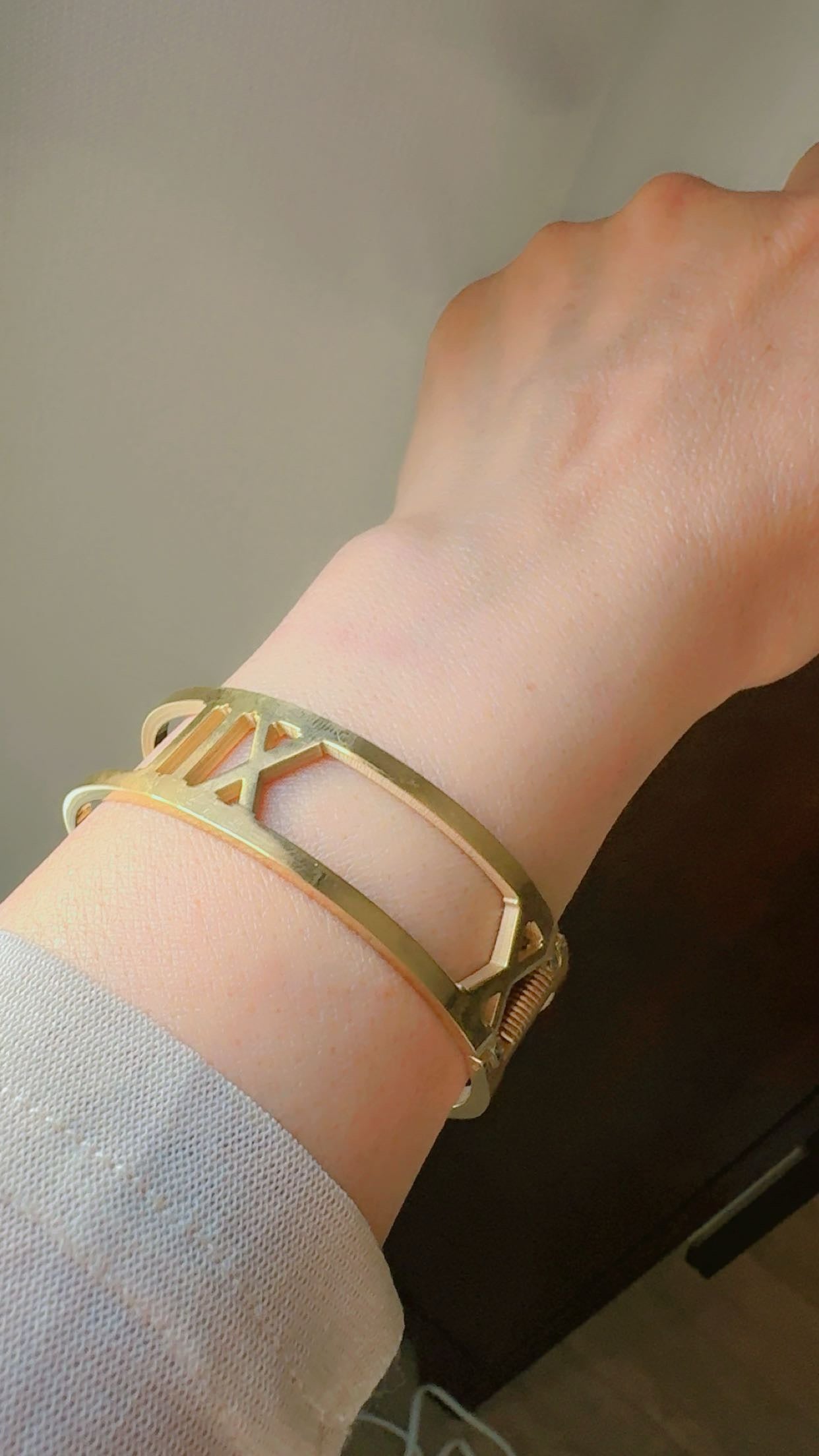 Gold bracelet on a wrist with a neutral background
