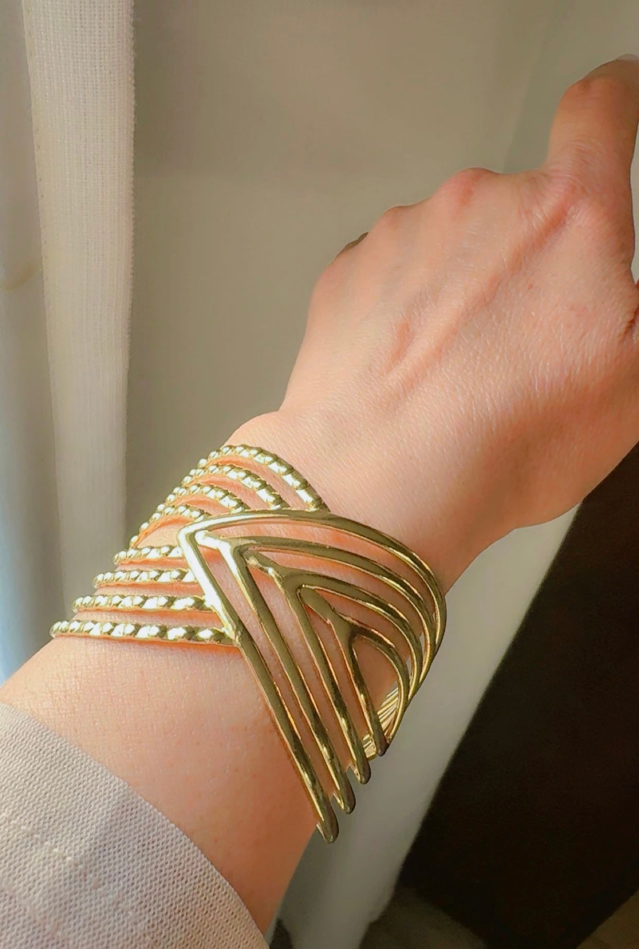 Gold cuff on a wrist with a neutral background