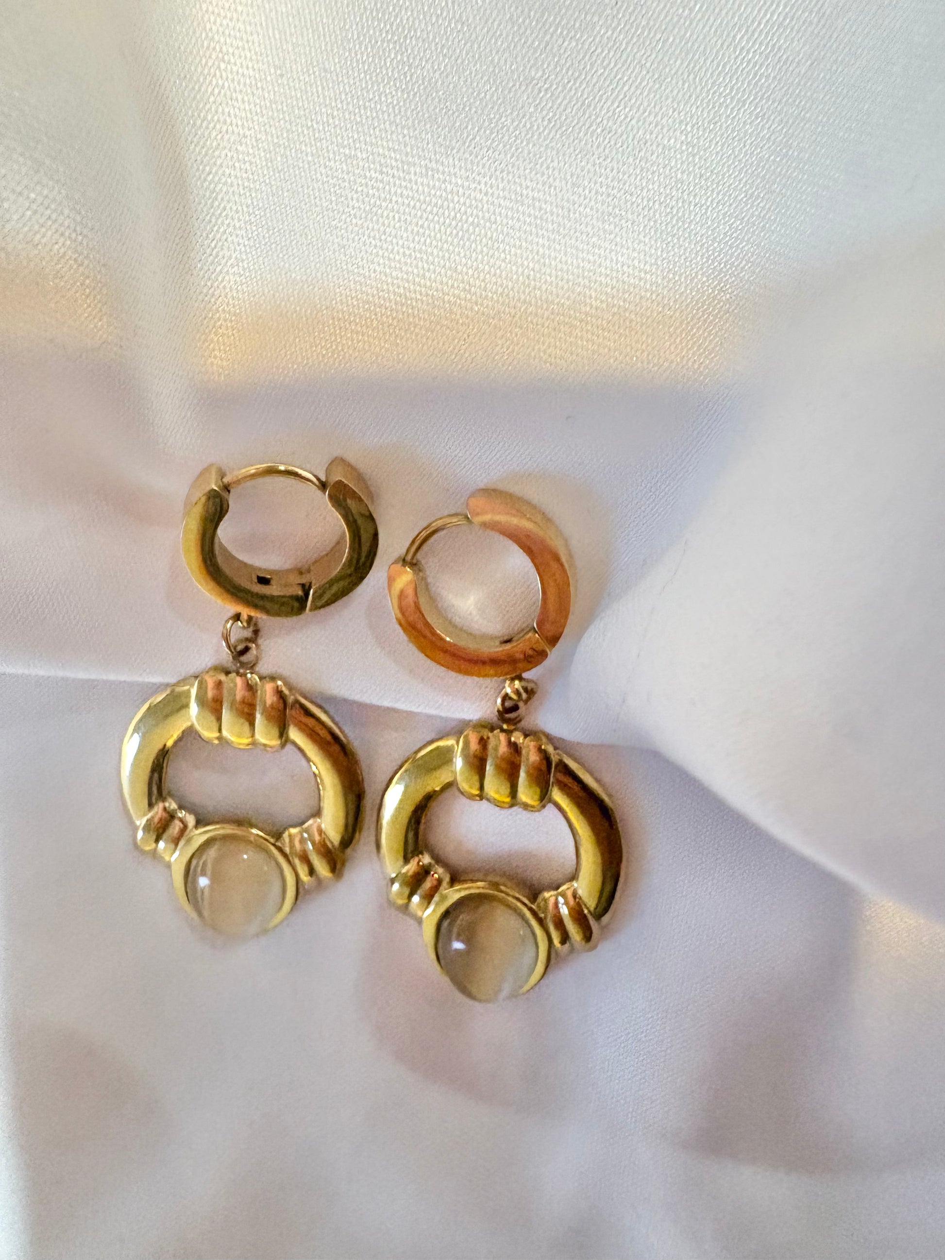 Gold hoop earrings with a central gemstone on a white fabric background