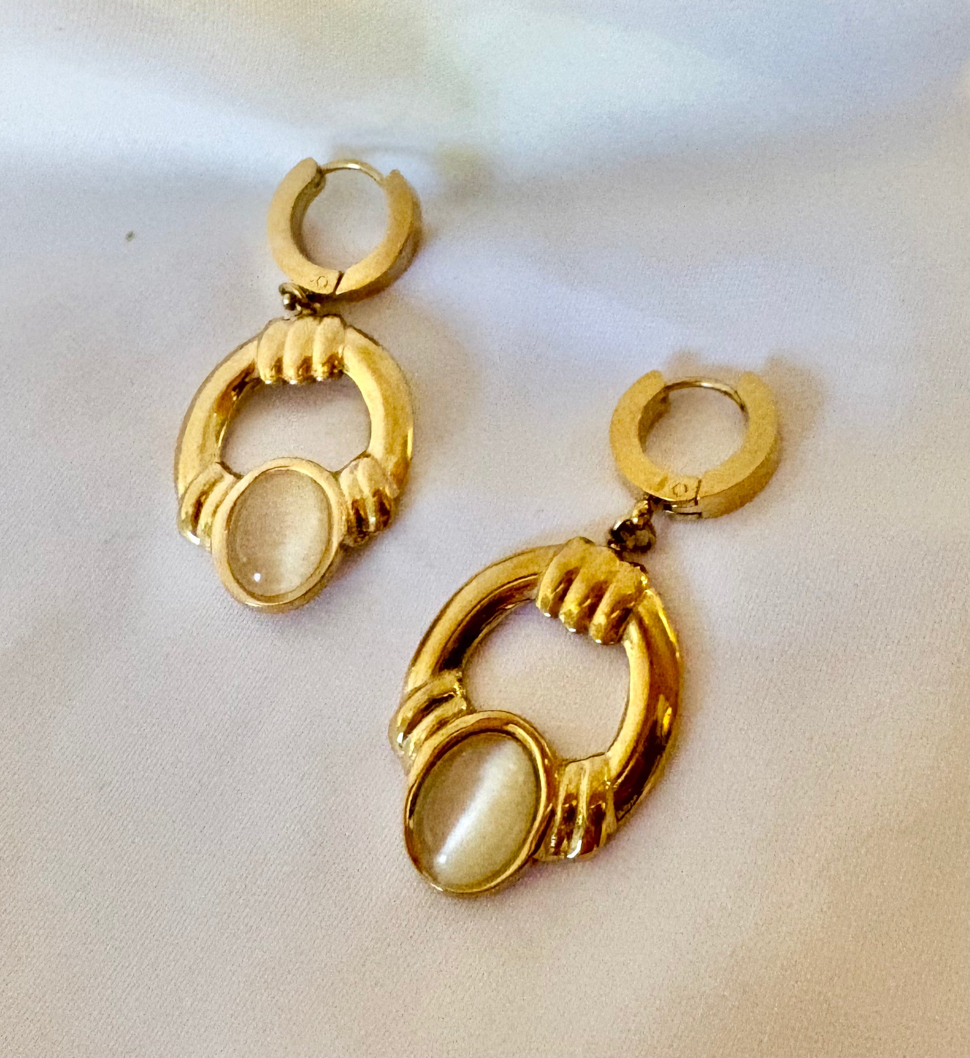 Pair of gold Oval hoop earrings with a central stone on a white background