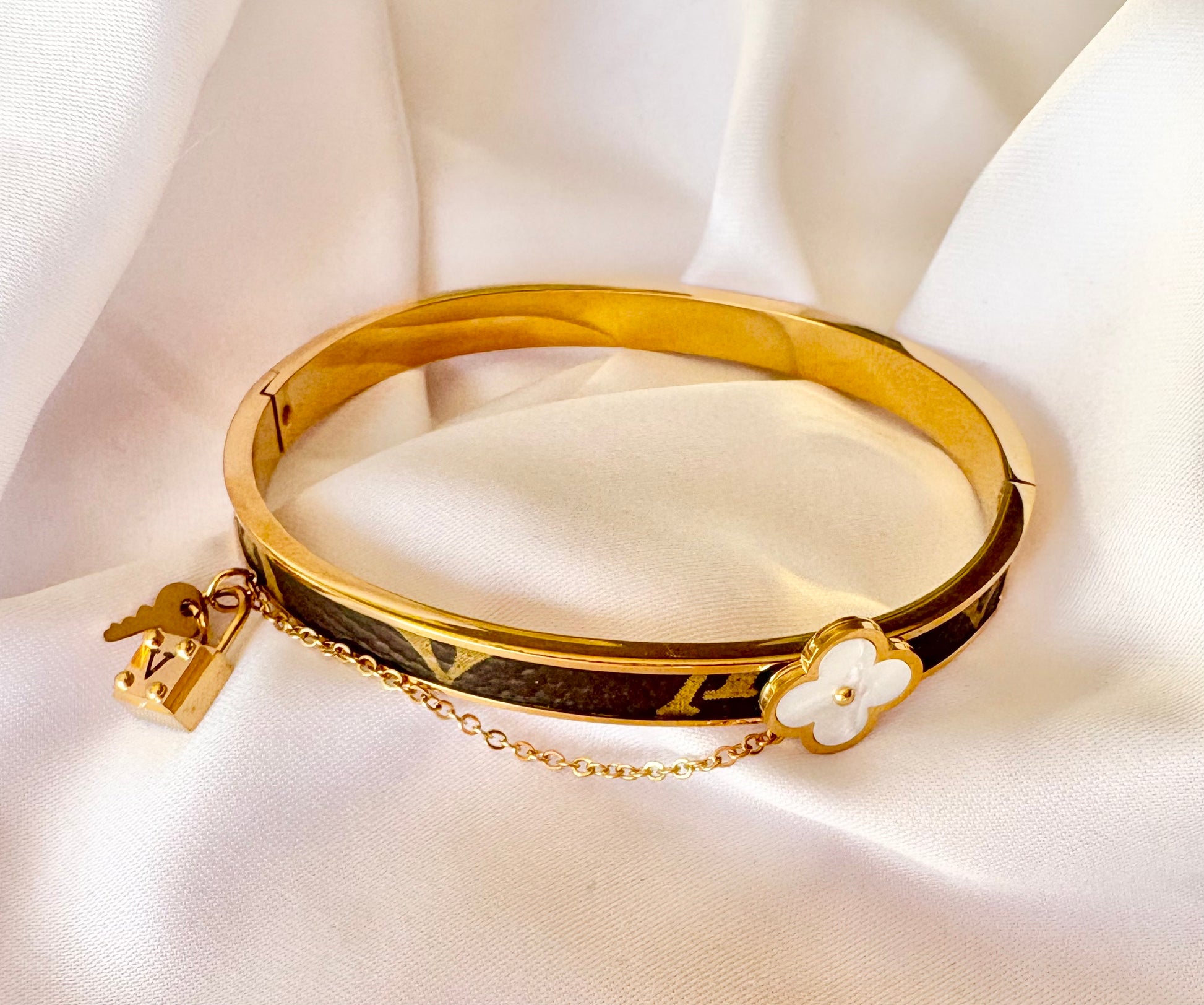 Gold bracelet with a floral charm on a white fabric background