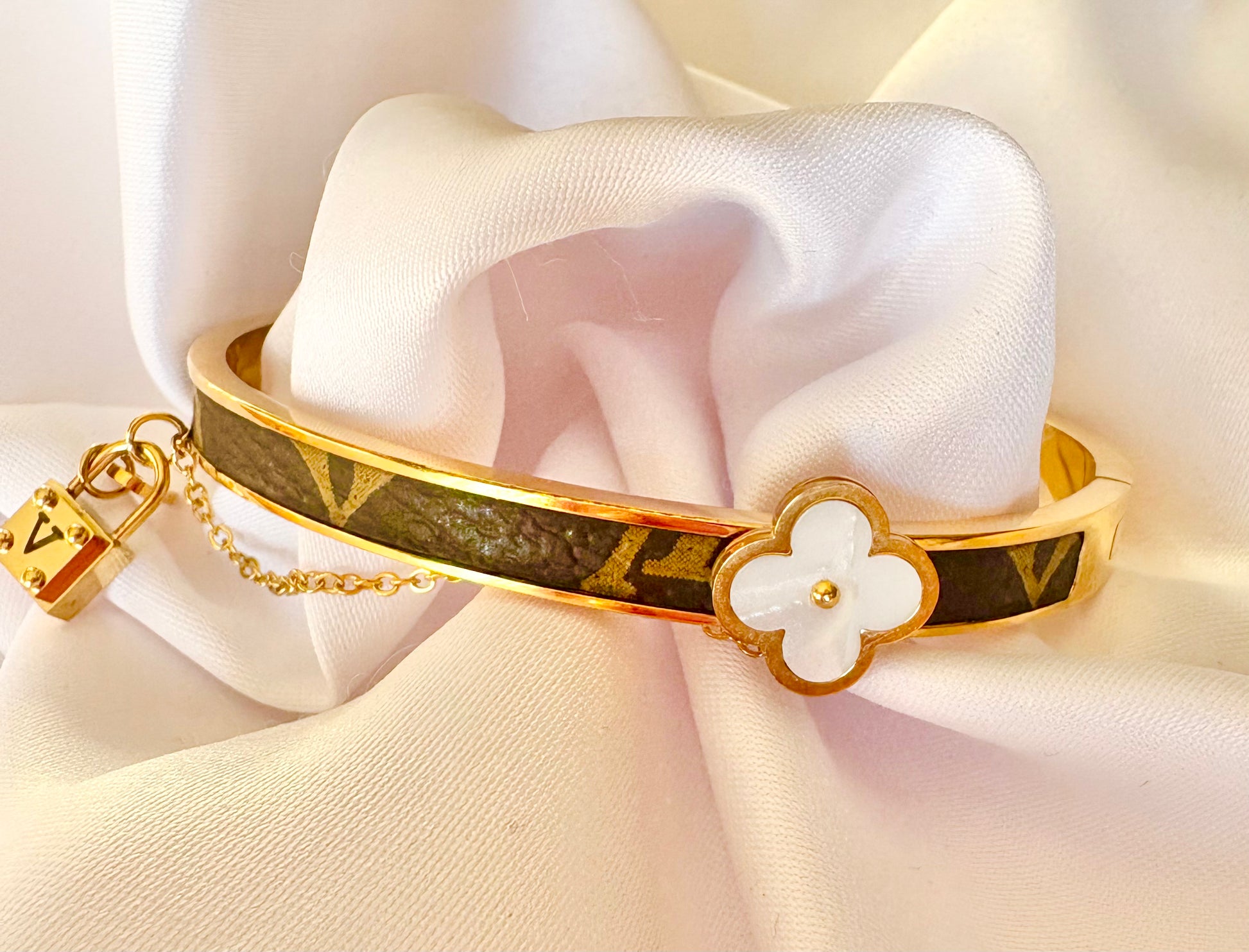 Gold bracelet with a floral charm on a white fabric background