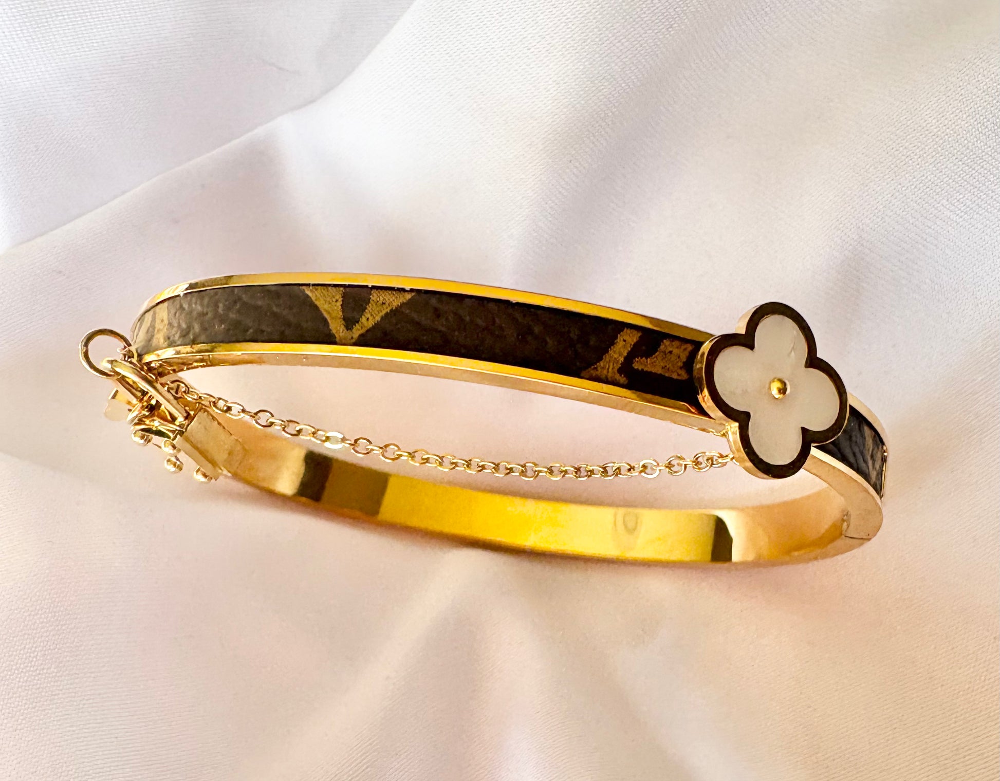 Gold bracelet with a black and gold flower clasp on a white fabric background