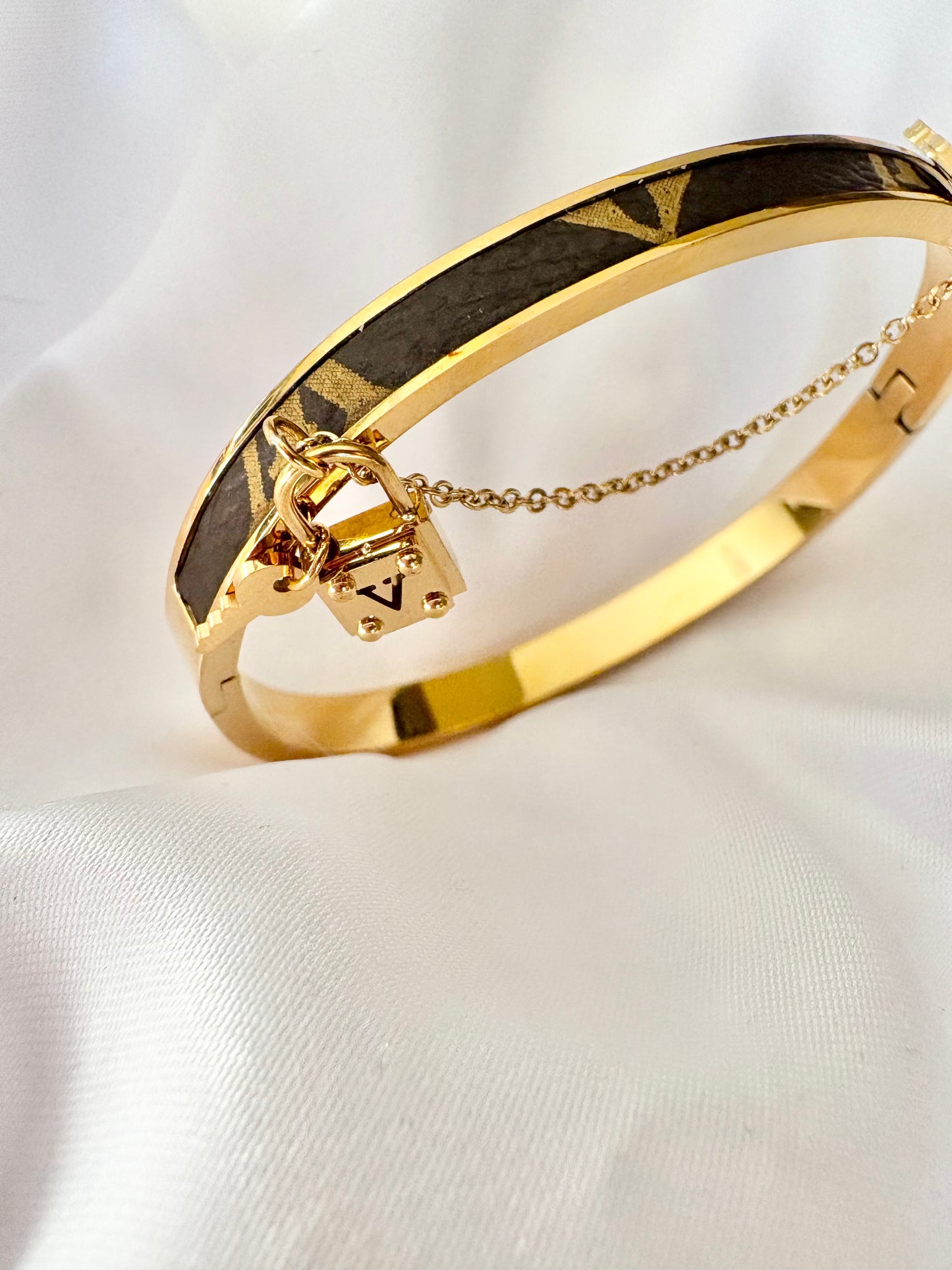 Gold bracelet with a padlock charm on a white fabric background