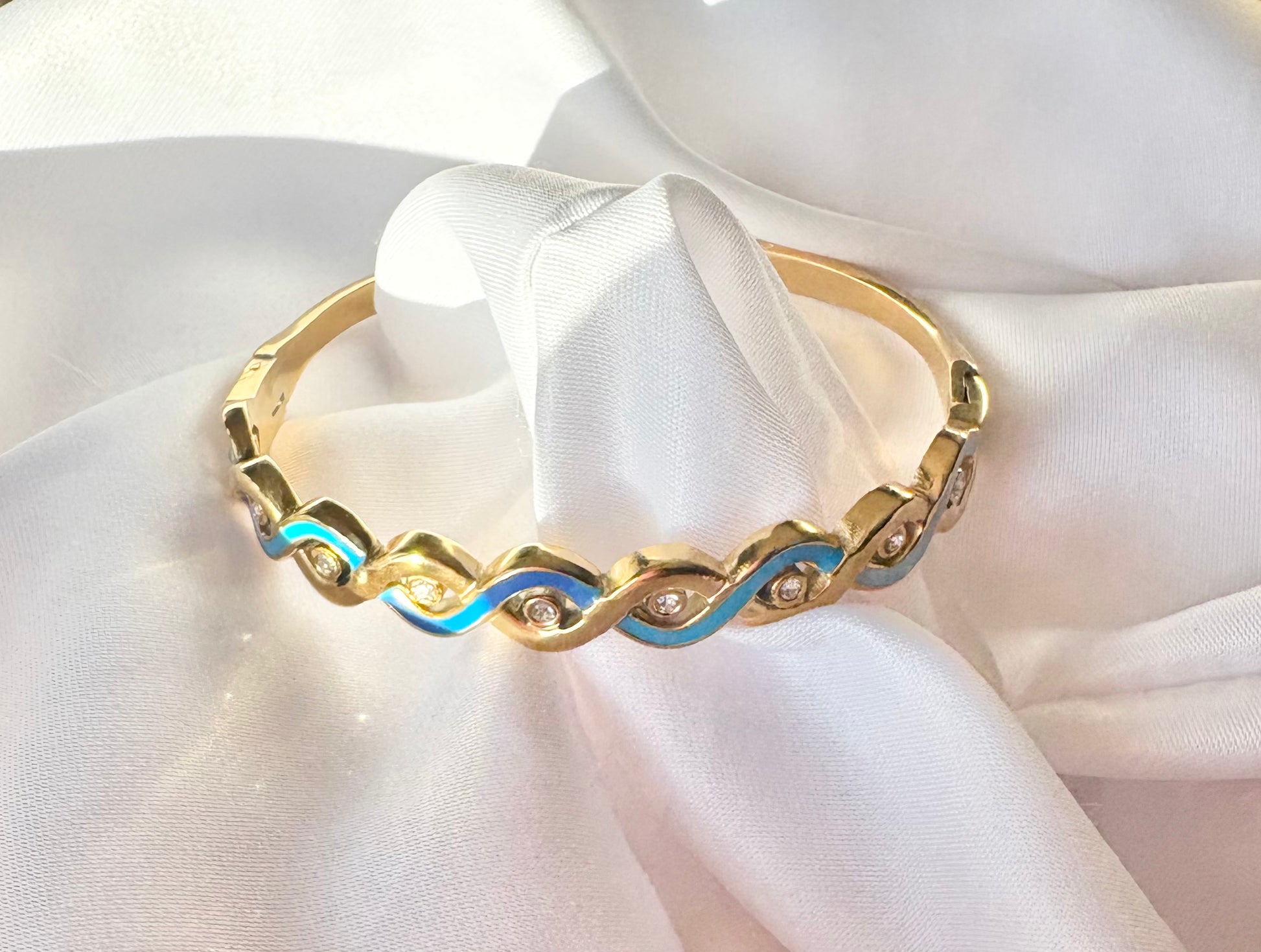 Gold bracelet with blue accents on a white fabric background