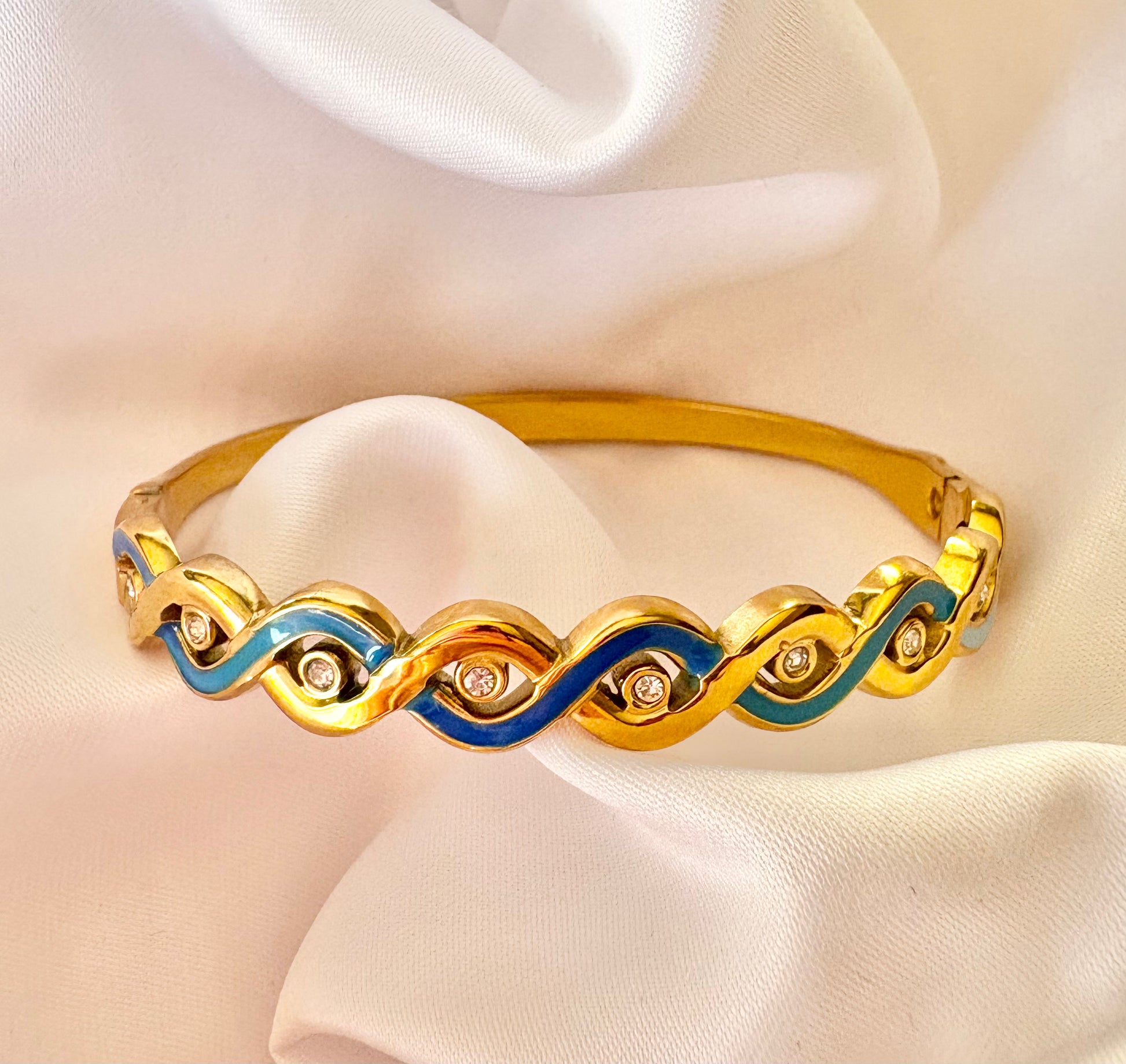Gold bracelet with blue accents on a white fabric background