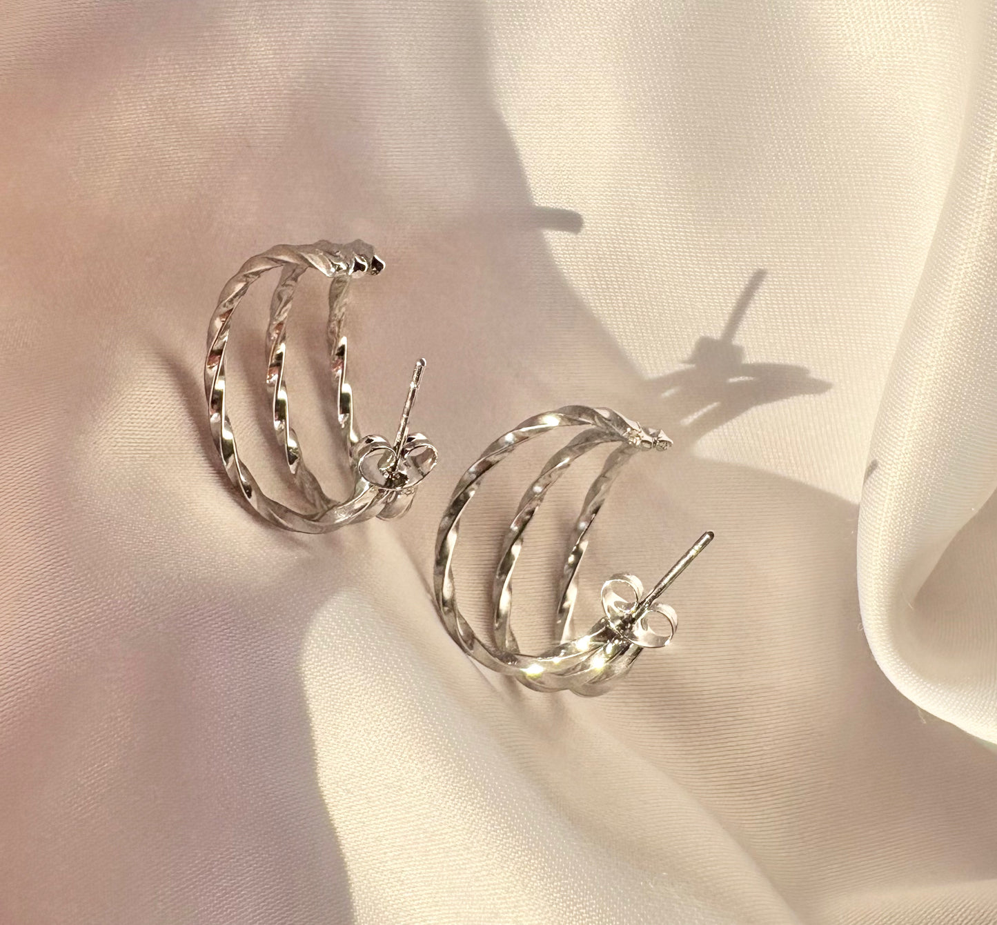 Silver hoop earrings on a soft beige fabric background