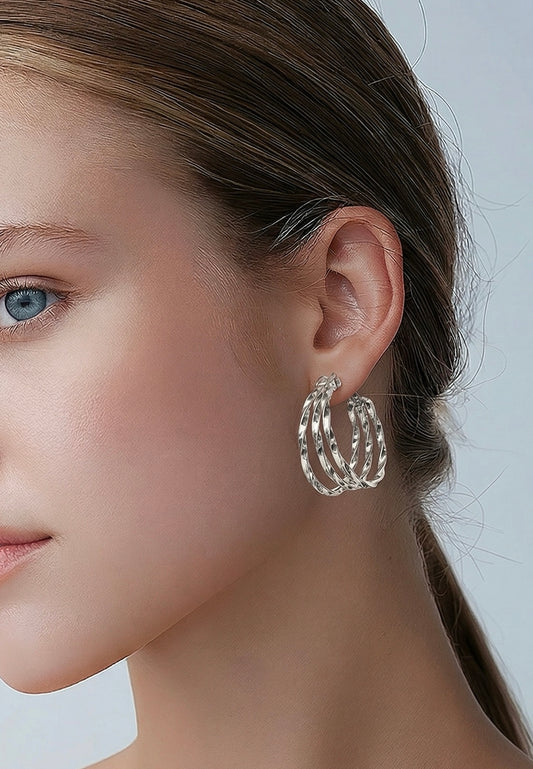 Close-up of a woman wearing silver hoop earrings with a neutral background