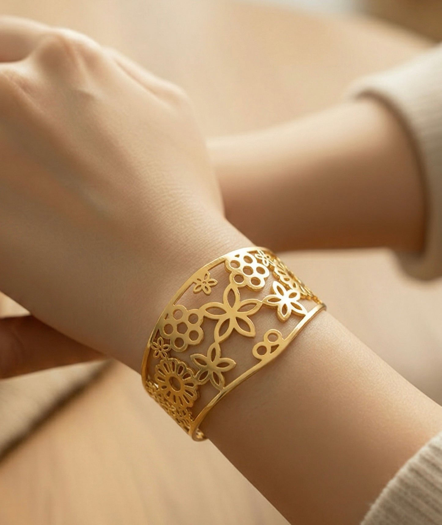 Gold bracelet with floral patterns on a wrist against a neutral background