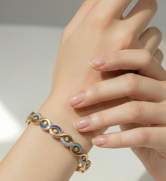 Gold bracelet with blue accents on a hand against a neutral background