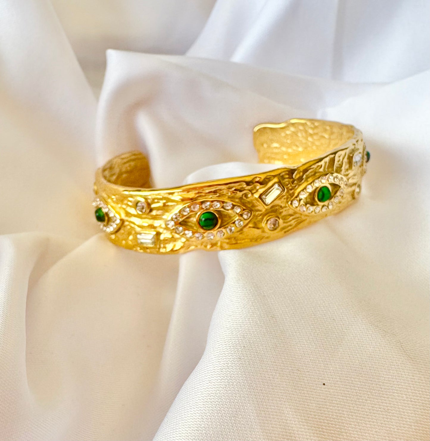 Gold bracelet with green gemstones on a white fabric background