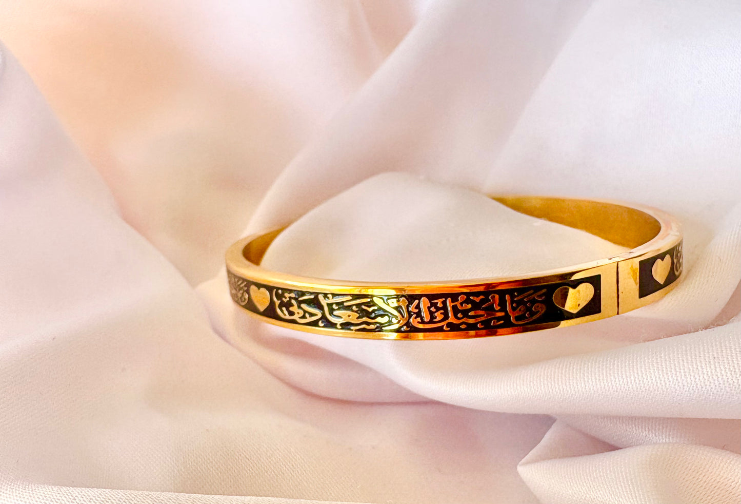 Gold bracelet with Arabic Calligraphy designs on a soft white fabric background