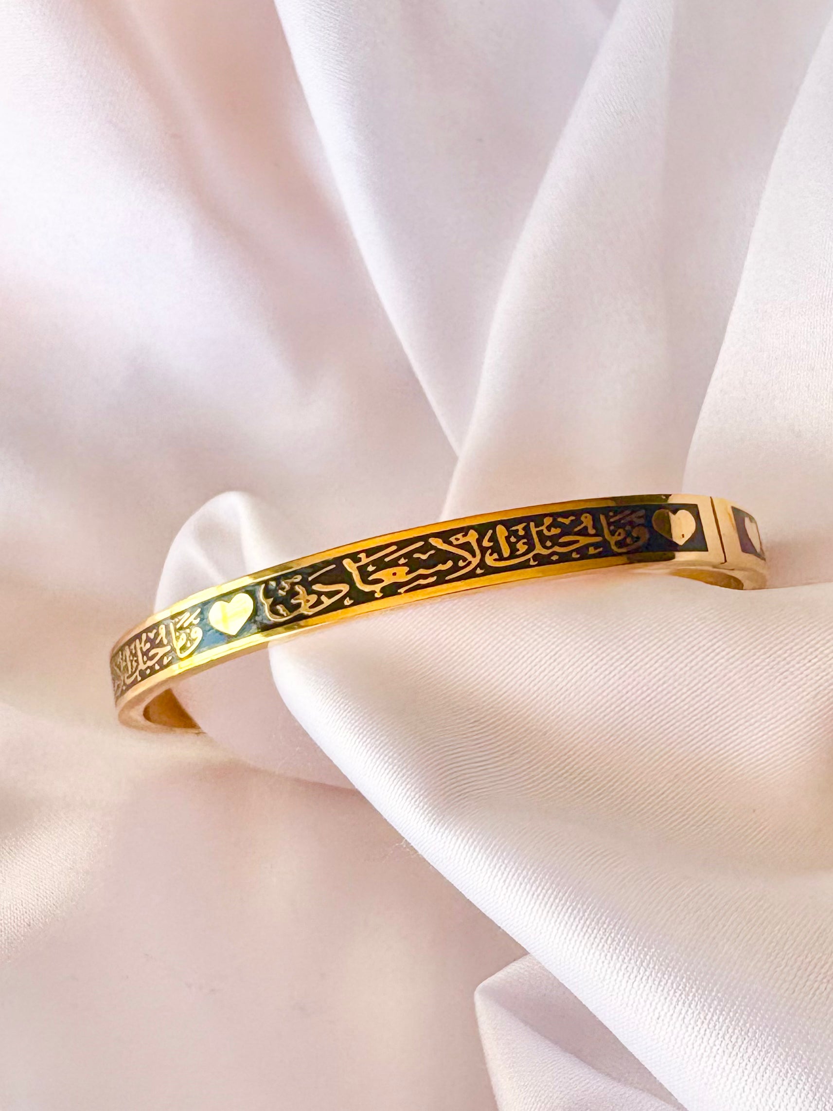 Gold bracelet with black engraved design on a white fabric background