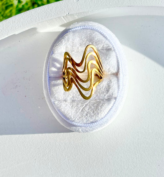 Gold wave-shaped ring on a white circular base 