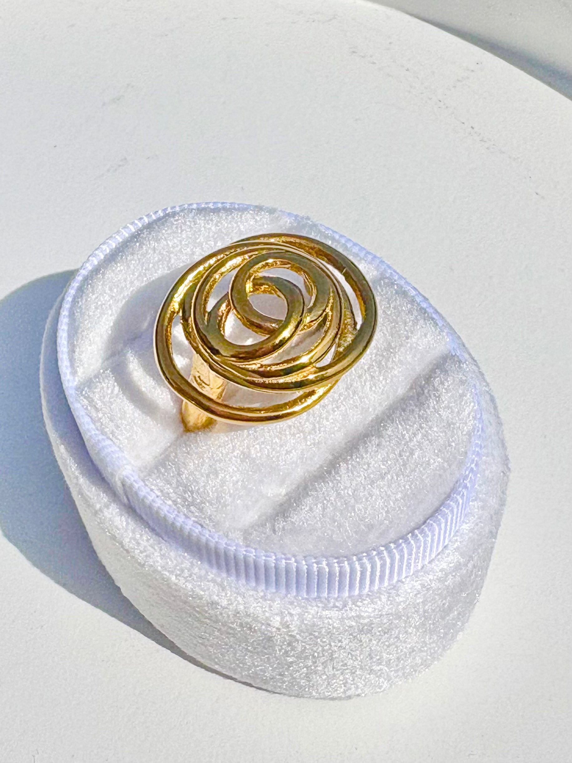 Gold spiral ring in a white jewelry box on a light gray background