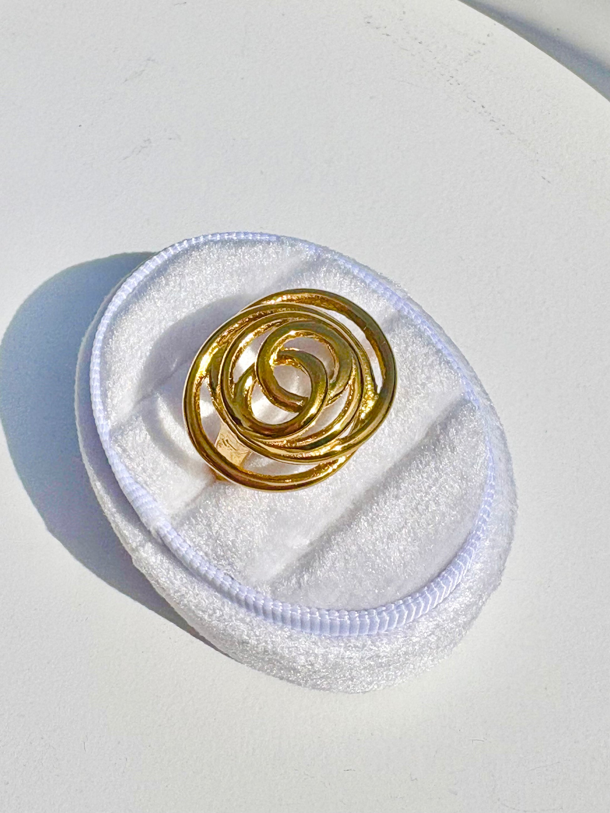 Gold spiral ring on a white cushion with a white background