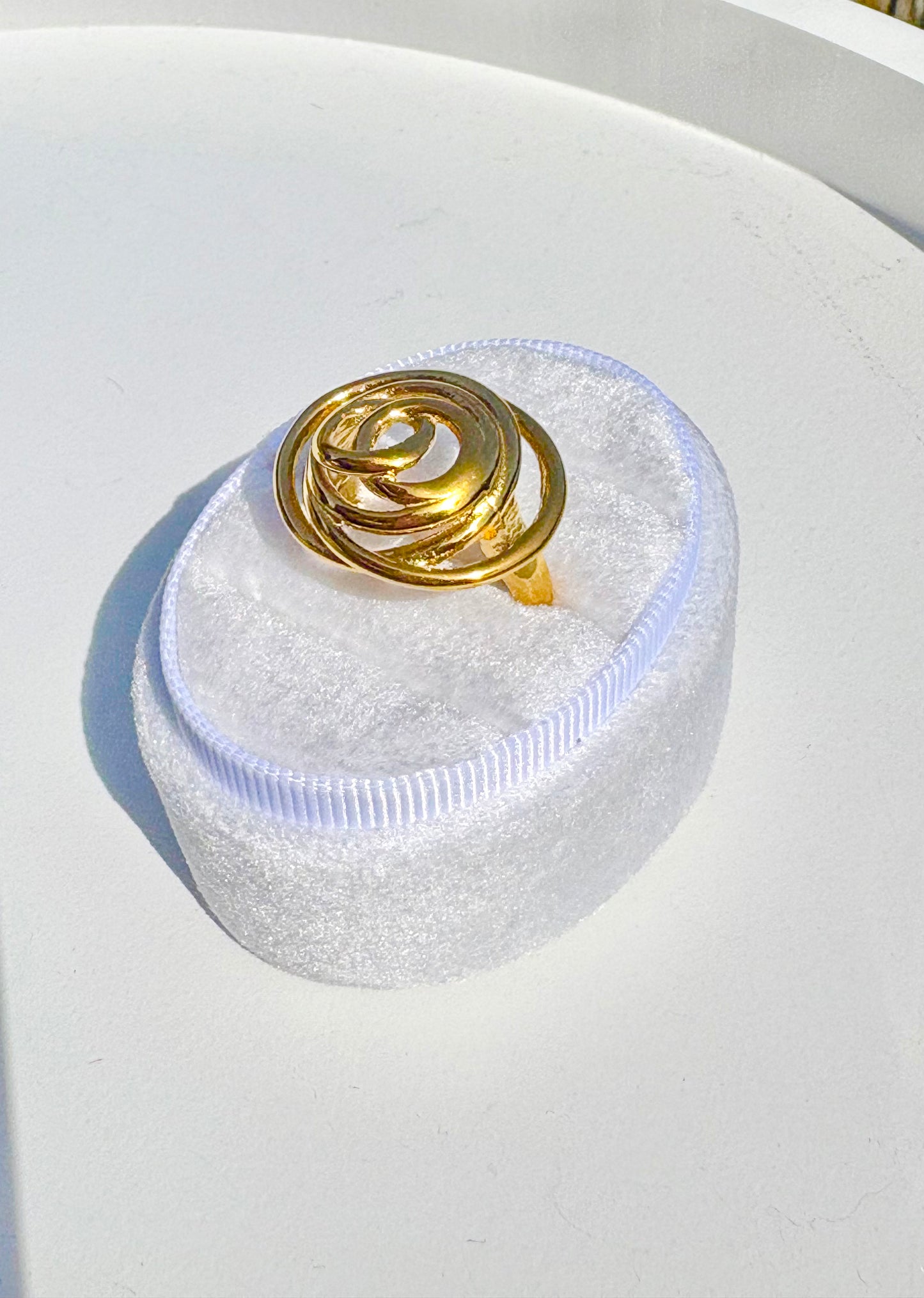Gold ring on a white cushioned stand with a light blue glow