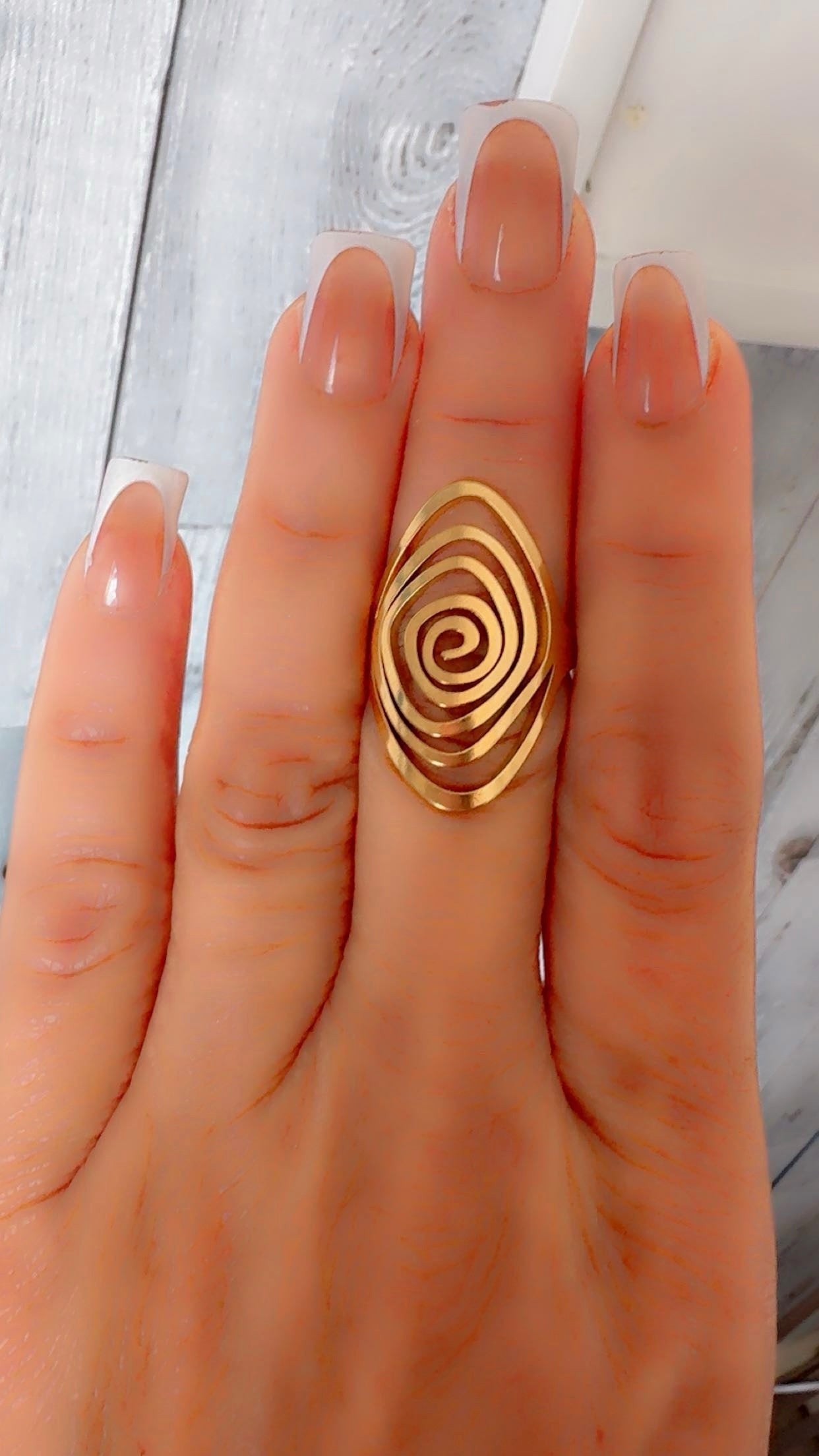 Gold spiral ring on a hand with a light wooden background