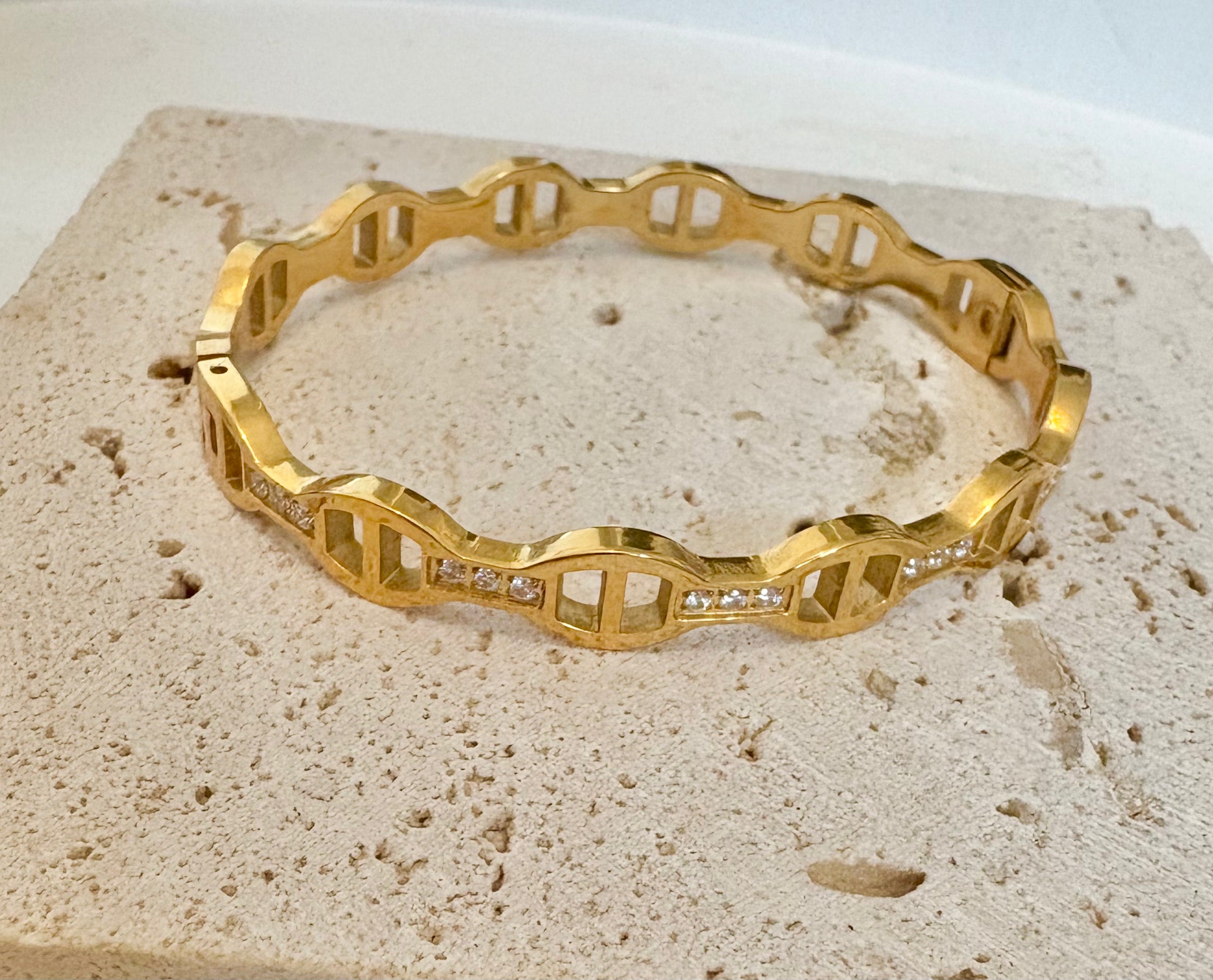 Gold bracelet with diamond accents on a textured beige surface
