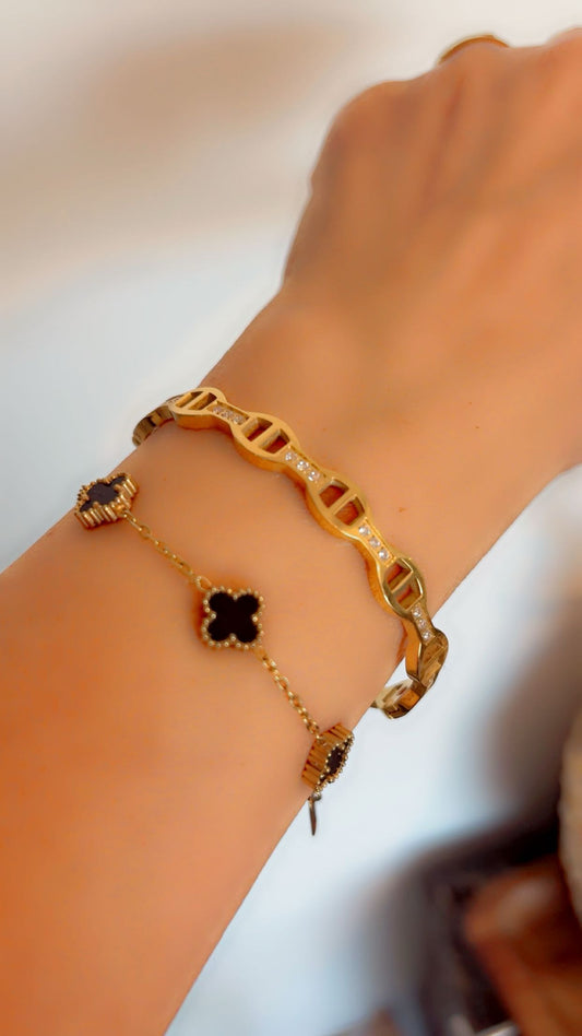Gold bracelet with clover-shaped charms on a wrist against a neutral background