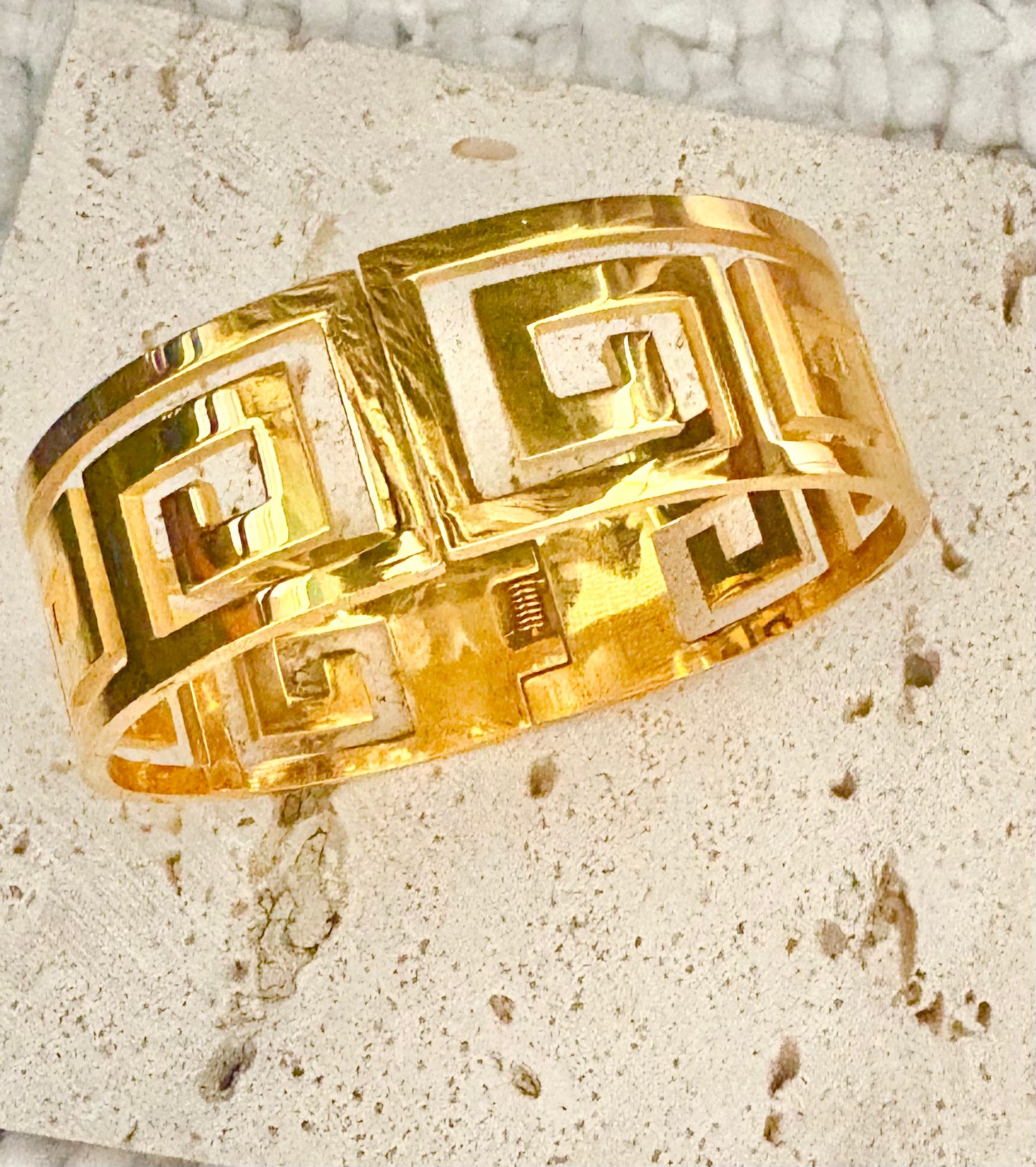 Gold bangle with intricate design on a textured surface