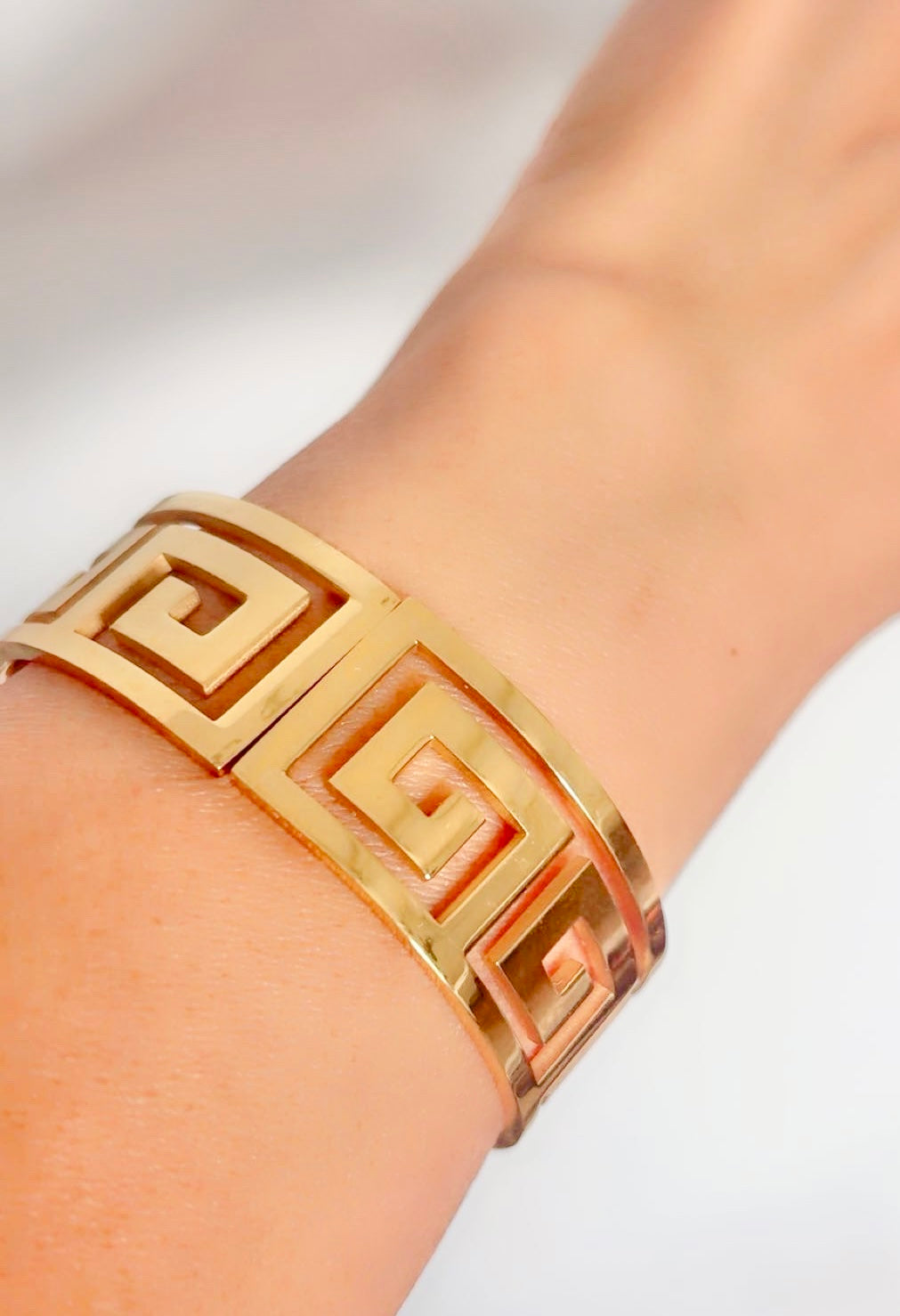 Gold bracelet with a geometric design on a wrist against a white background