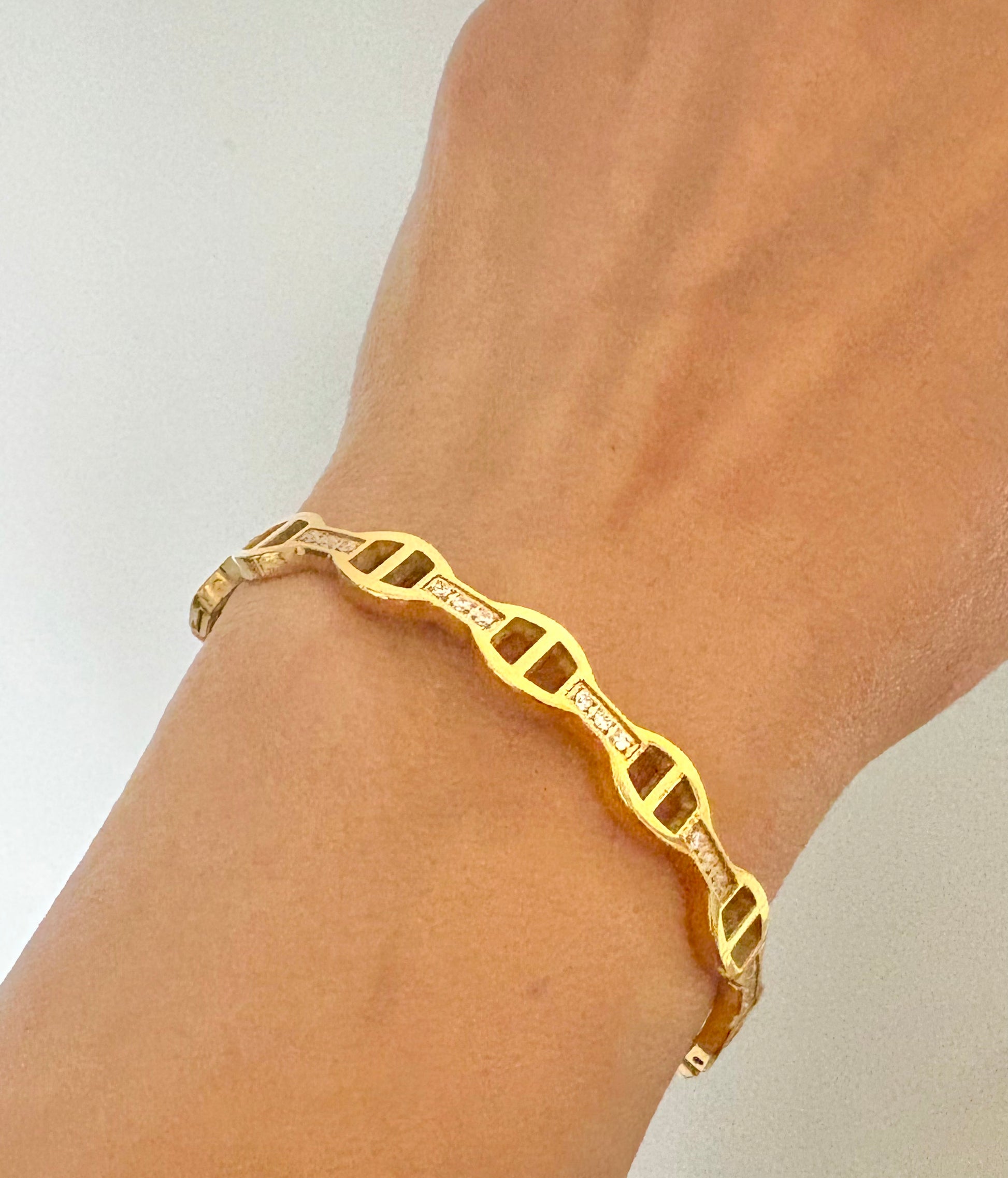 Gold bracelet on a wrist with a plain background