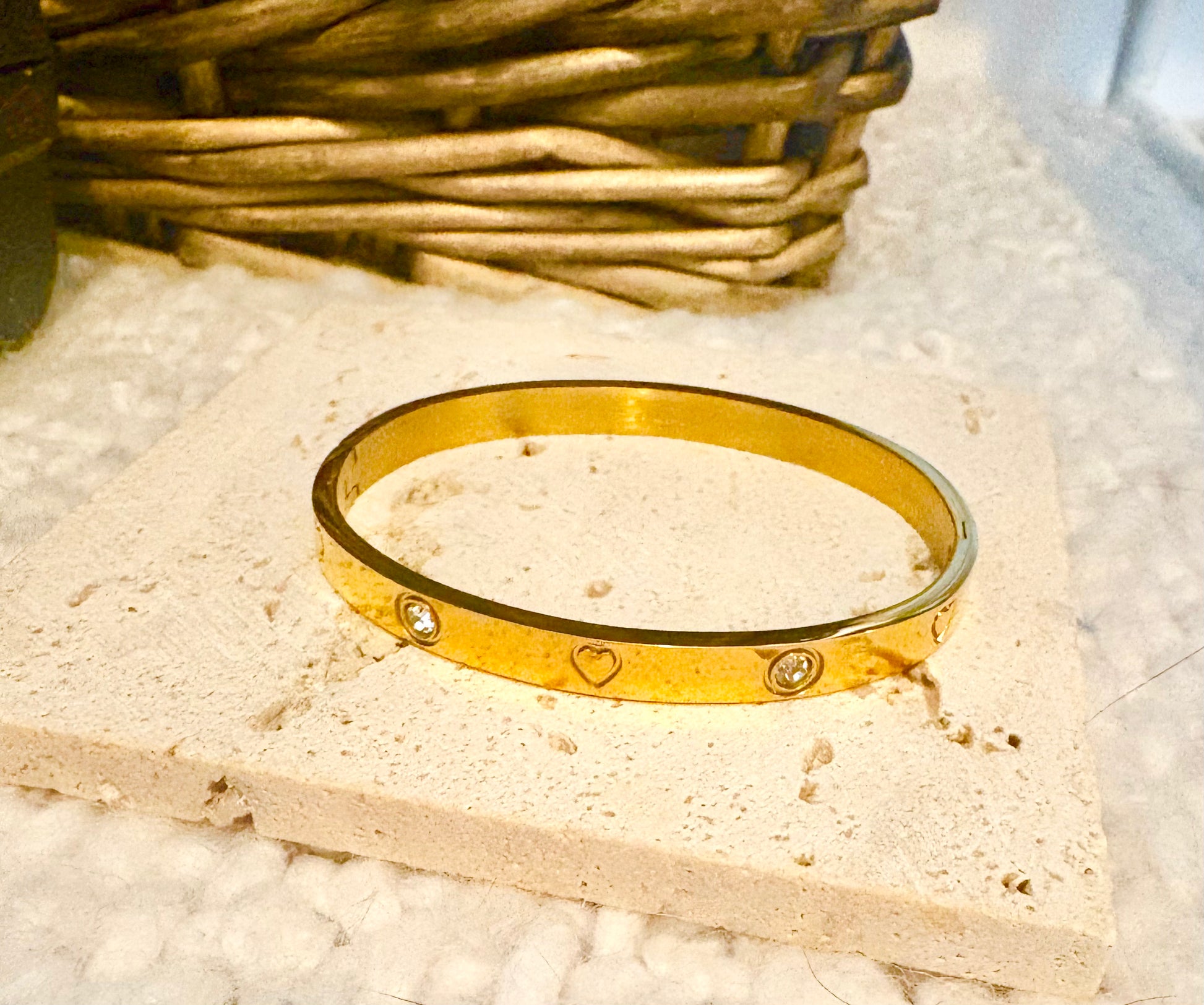 Gold bracelet with heart and diamond designs on a textured surface