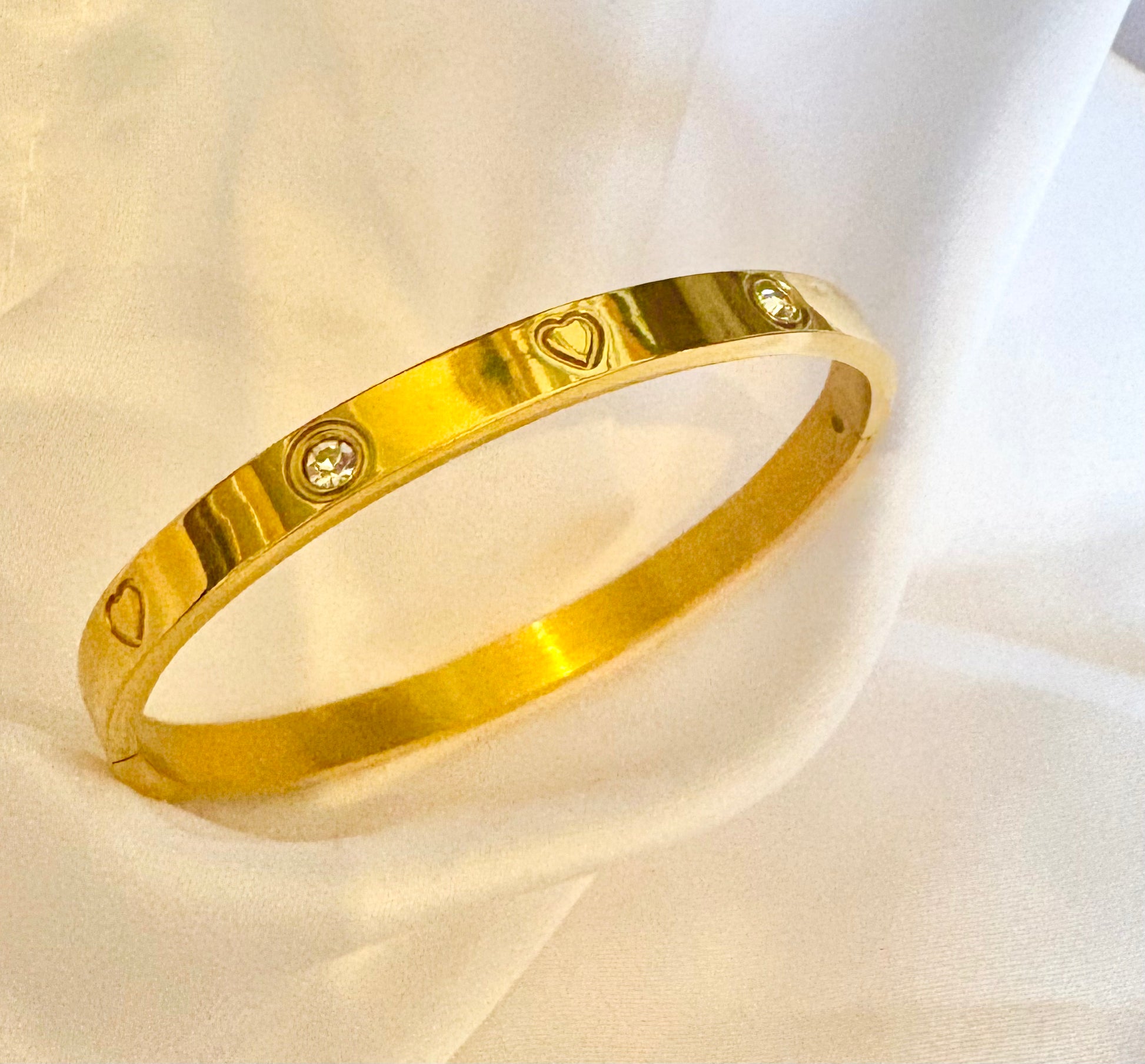 Gold bracelet with heart and diamond designs on a light fabric background