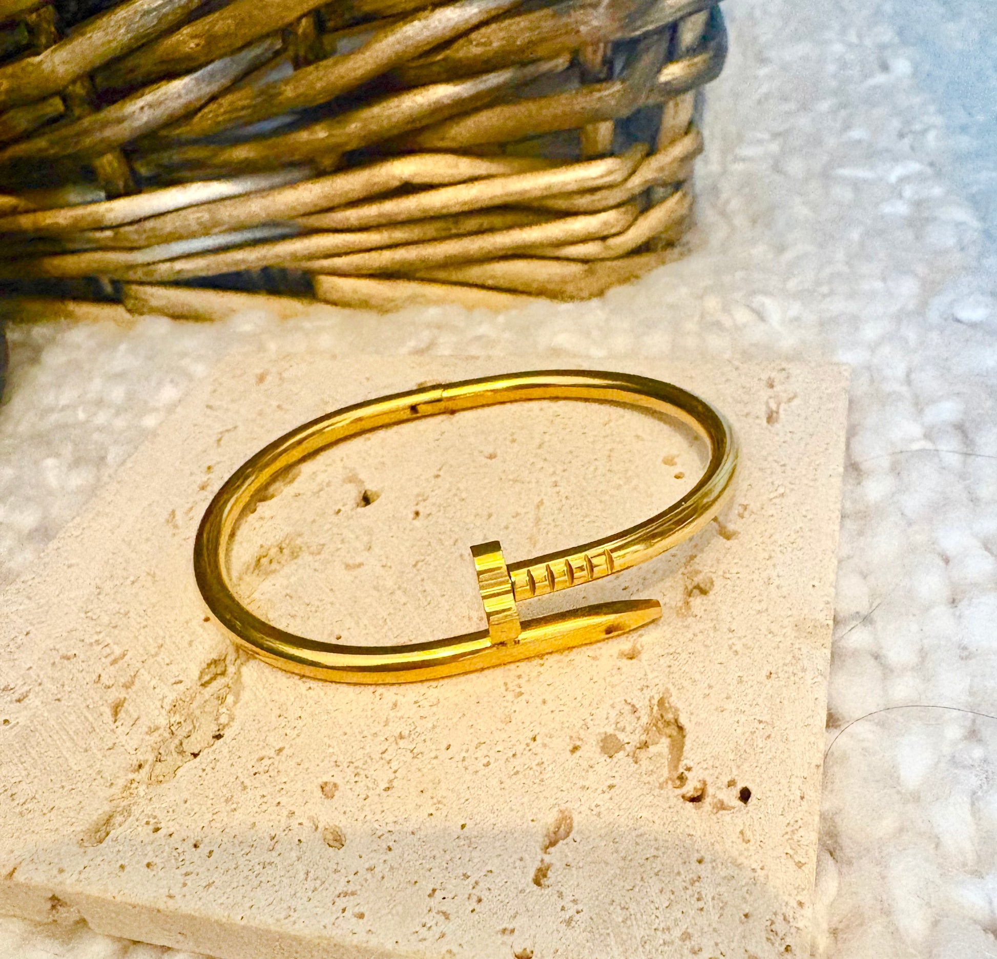 Gold bracelet on a textured stone surface with a woven basket in the background
