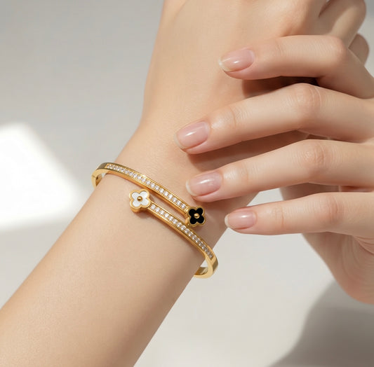 Gold bracelet with a black flower charm on a wrist against a neutral background