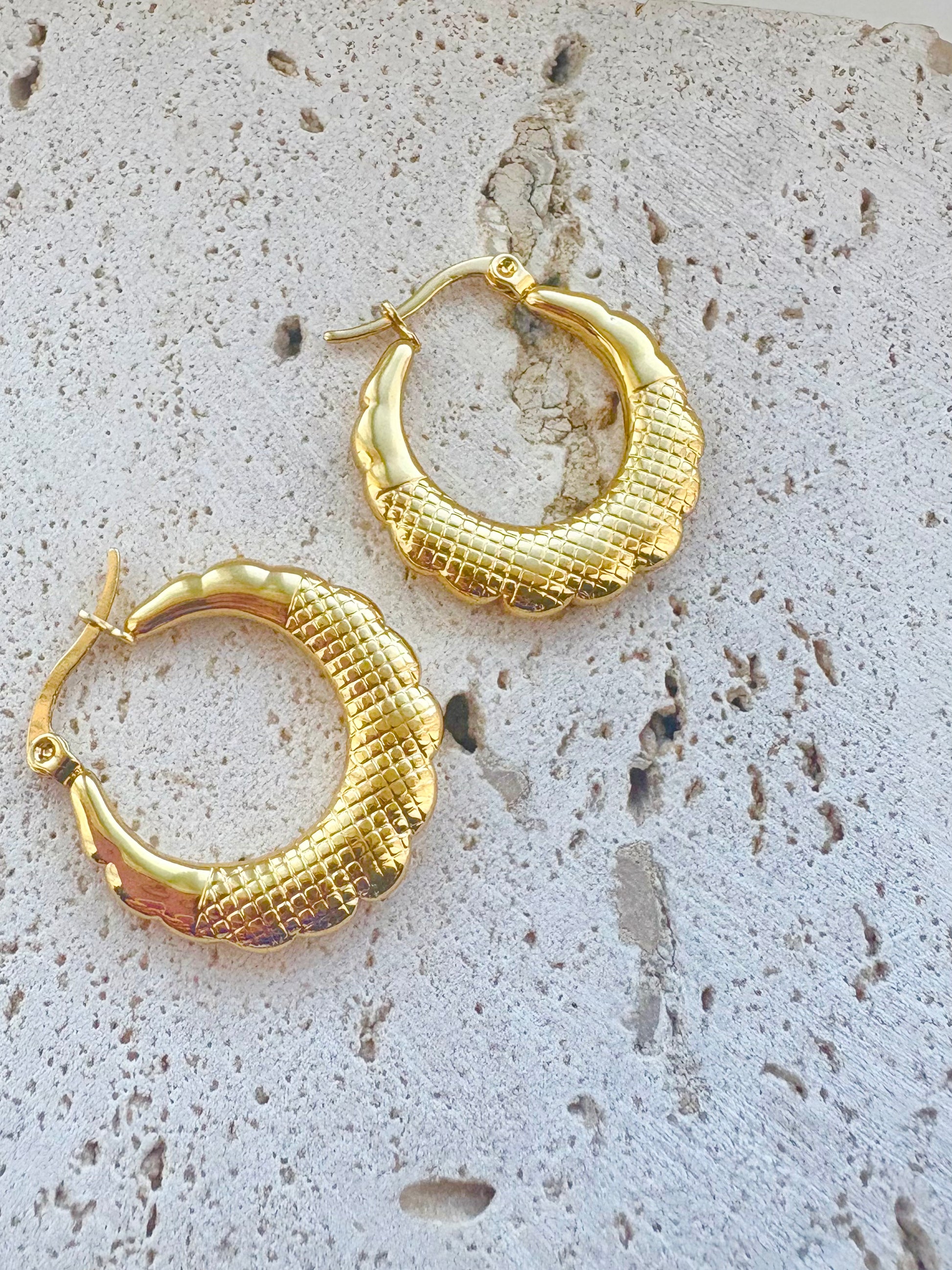 Gold hoop earrings on a textured stone surface