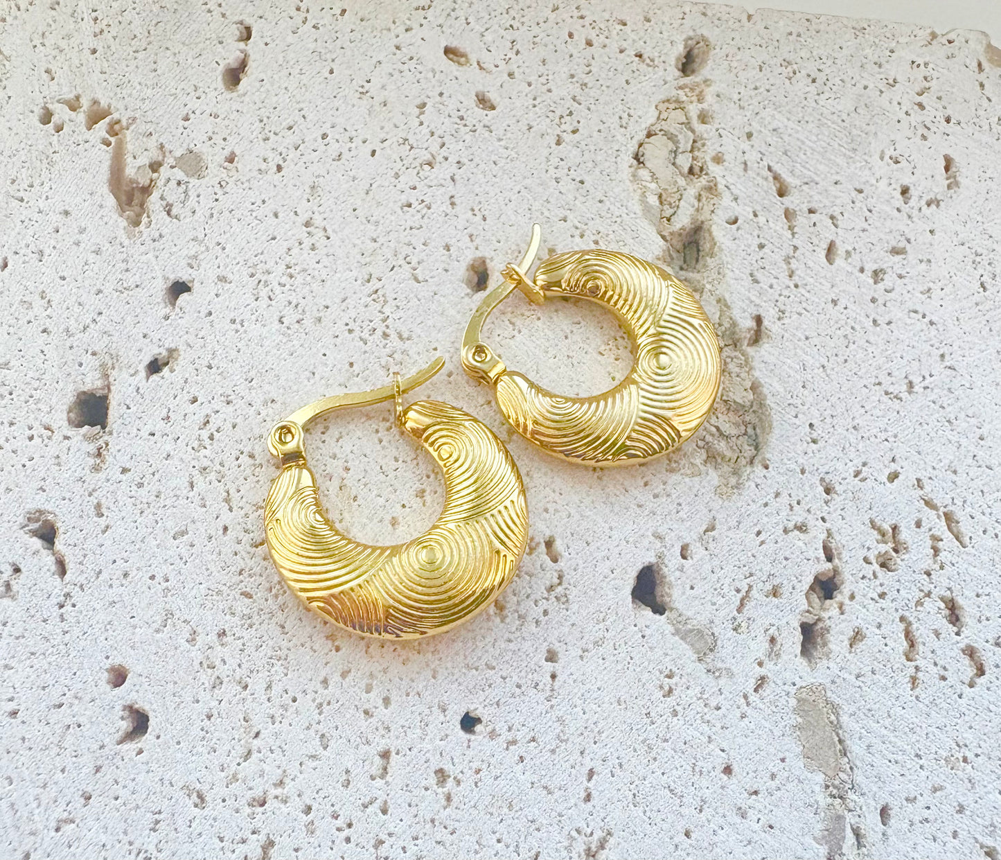 Gold hoop earrings on a textured stone surface